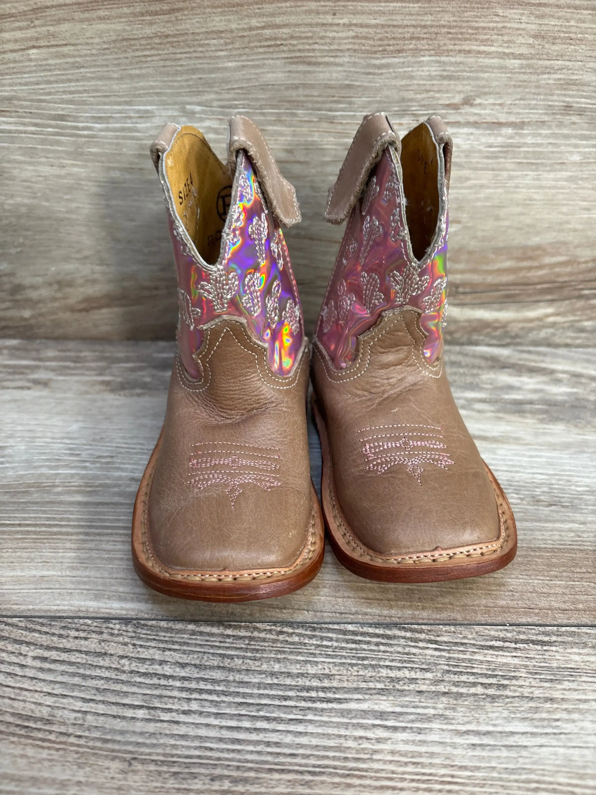 Front view of Roper toddler cowgirl boots size 4C showing iridescent pink cactus-stitched shafts and tan leather toes on wood background