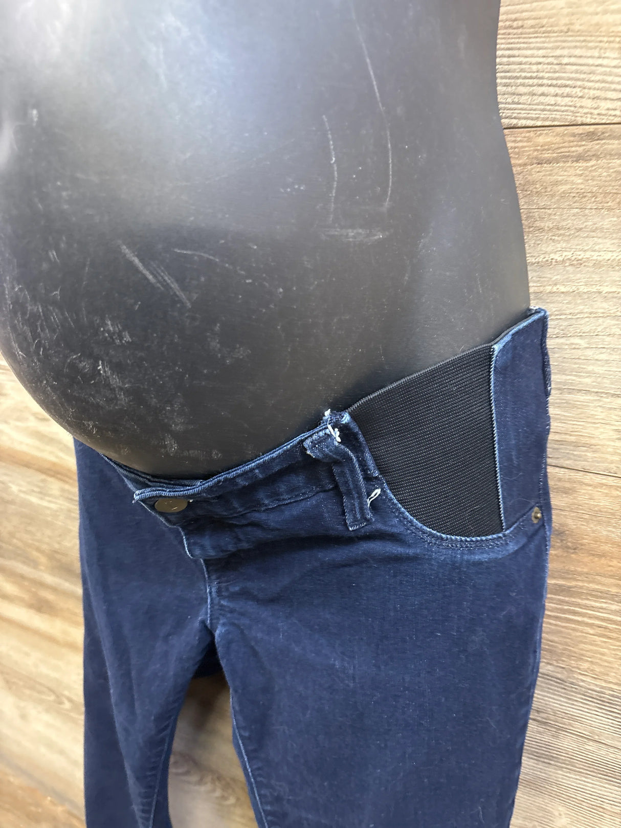 Side close-up of blue Isabel maternity side-panel jeggings with elastic side panel and button closure on wood background