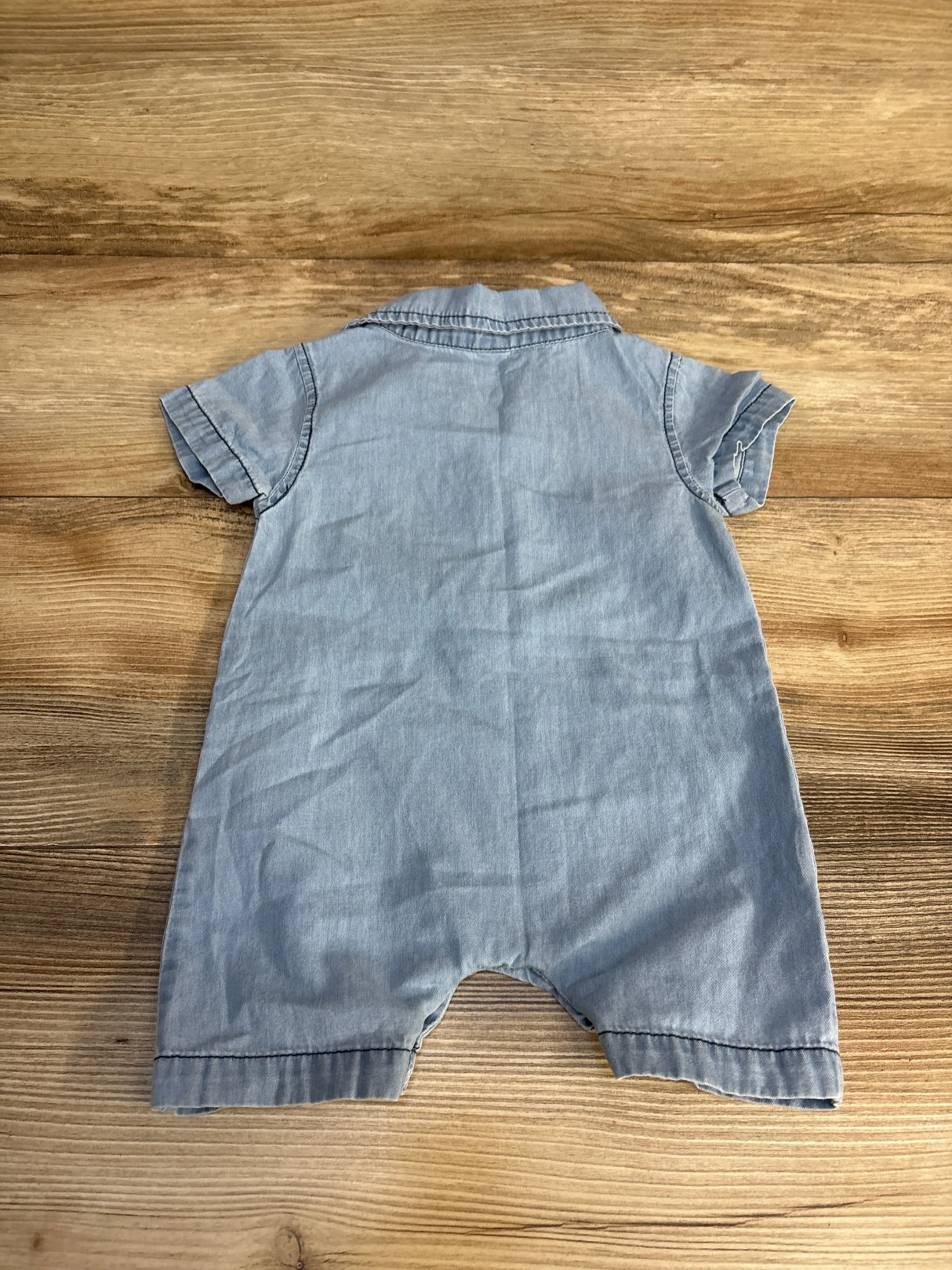 Light blue denim baby romper with short sleeves, laid on wooden surface