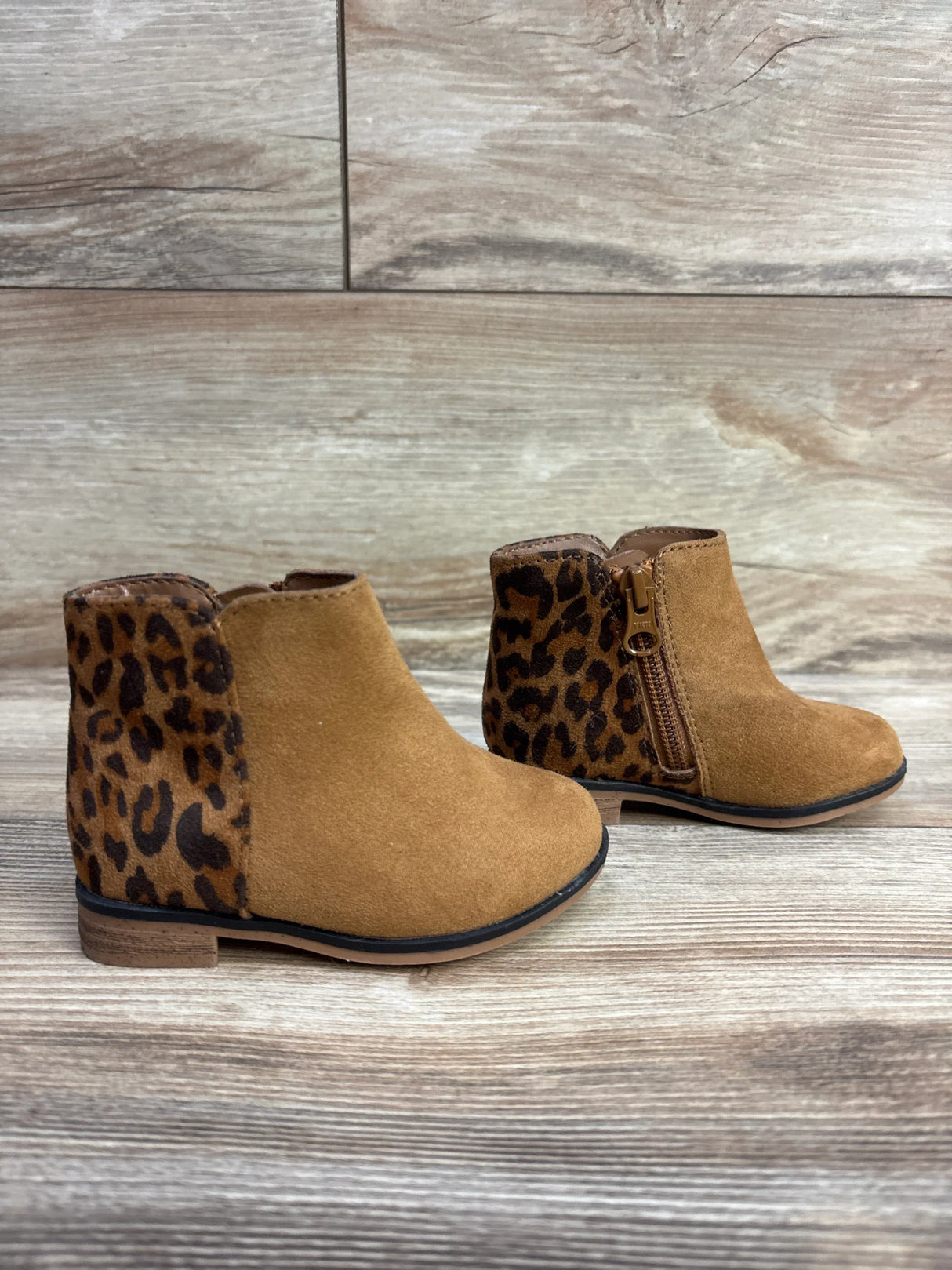 Pair of toddler brown suede ankle boots with leopard print heel and side zipper on wooden floor