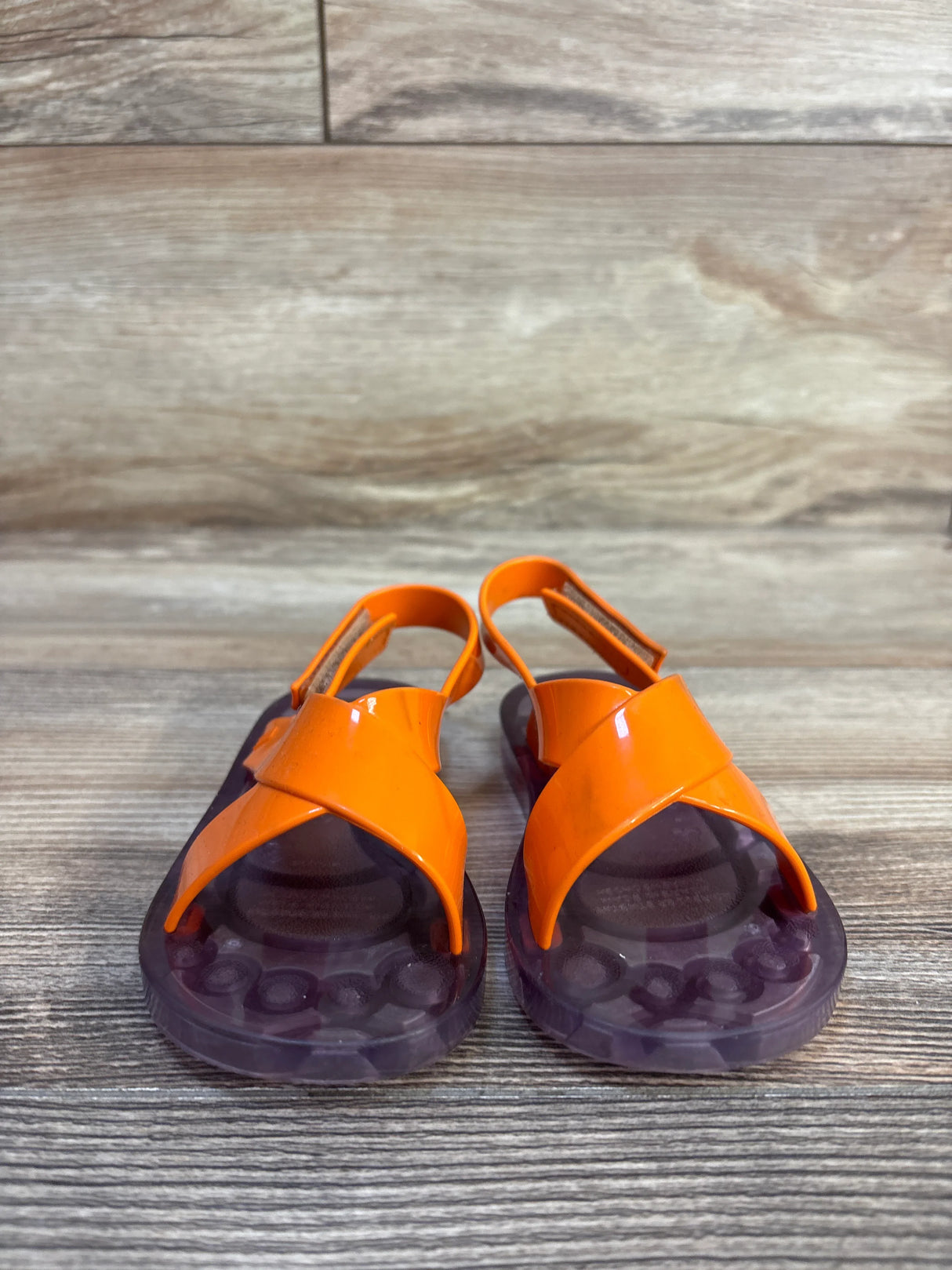 Orange toddler jelly sandals with purple soles on wood background