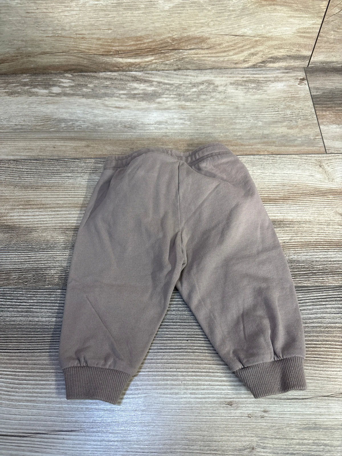 Flat lay of H&M brown baby jogger pants (3 months) showcasing back view, elastic waistband, and ribbed cuffs on wood background