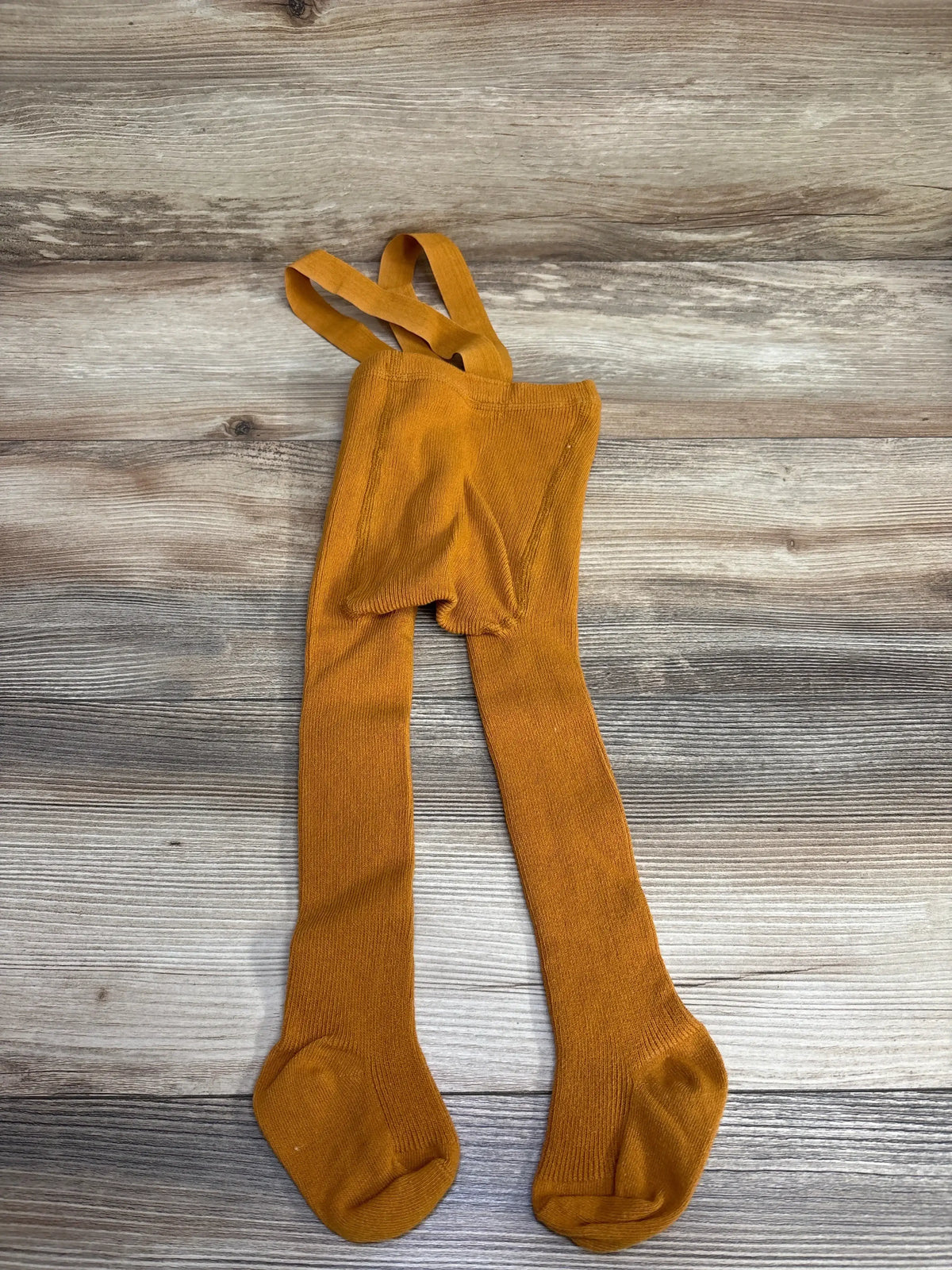 Rust orange toddler knit tights with suspenders on wood background