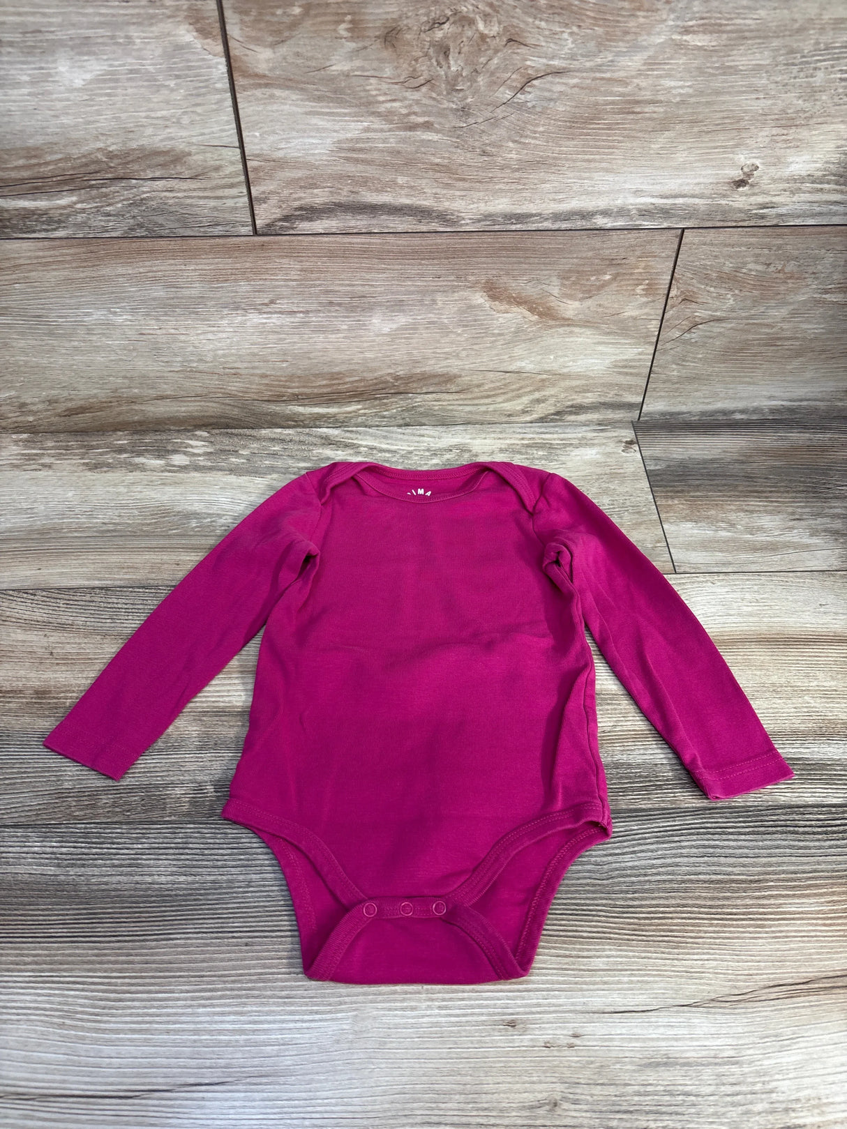 Magenta long sleeve baby onesie on wooden background