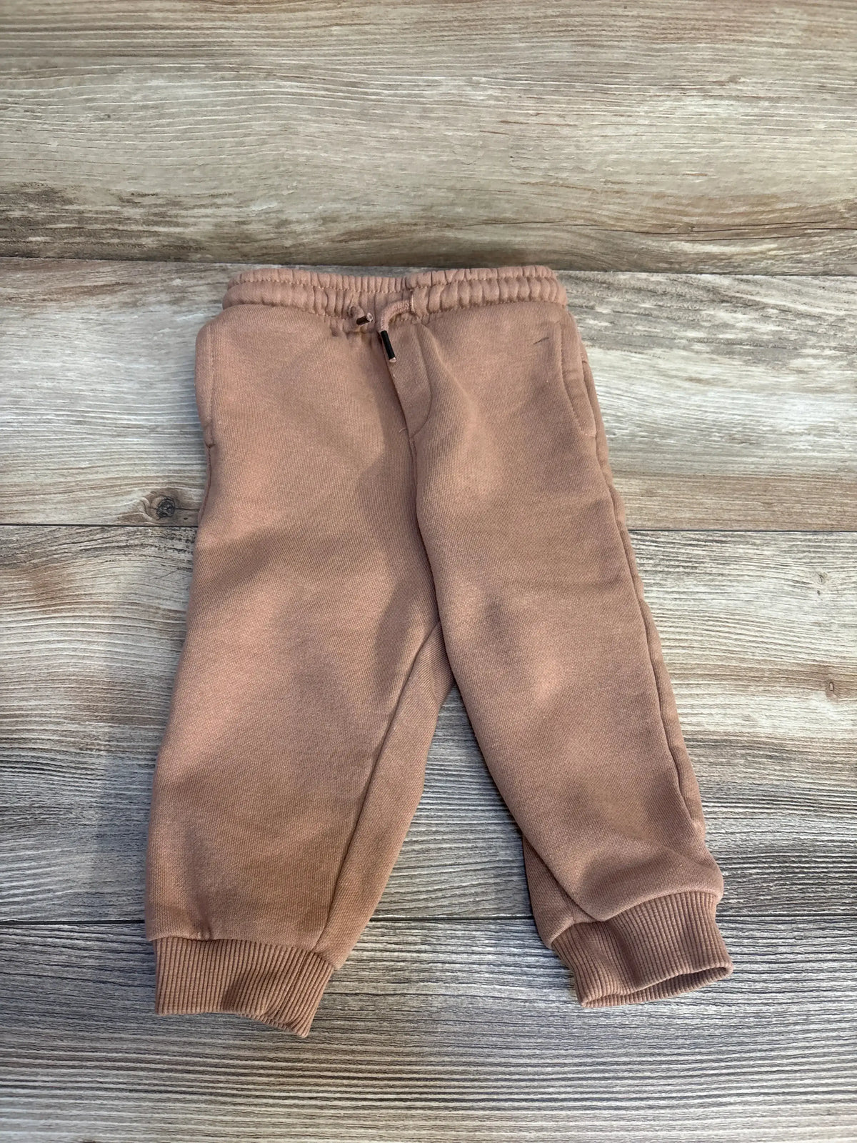 Flat lay of Boys Orchestra tan joggers (12 months) showing elastic drawstring waistband and ribbed cuffs on wooden floor background