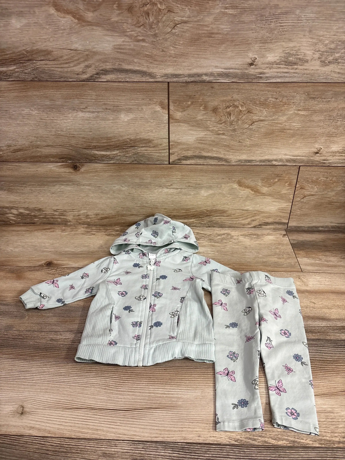 Flat lay of Haute Hippie 2pc Butterfly Print Zip-Up Hoodie and Pants Set in mint green size 3-6m showcasing matching butterfly print on wood plank floor