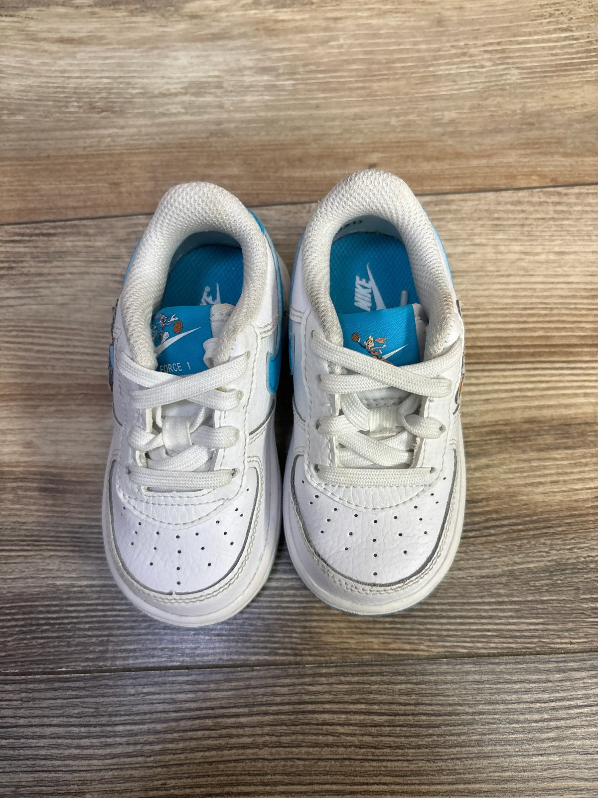 Top view of Nike Air Force 1 TD x Space Jam Hare sneakers showcasing mismatched Bugs Bunny and Lola Bunny details on a wood floor
