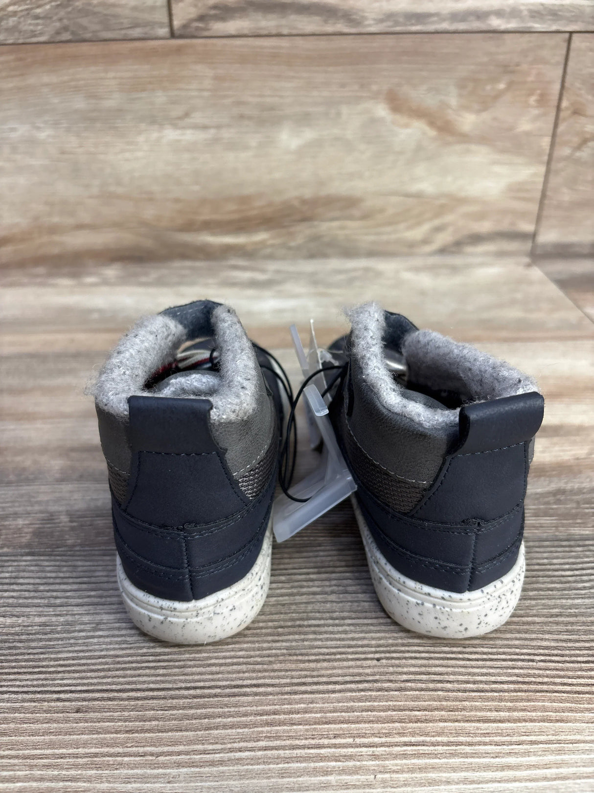 Back view of black and gray kids winter boots with white speckled soles on wooden floor