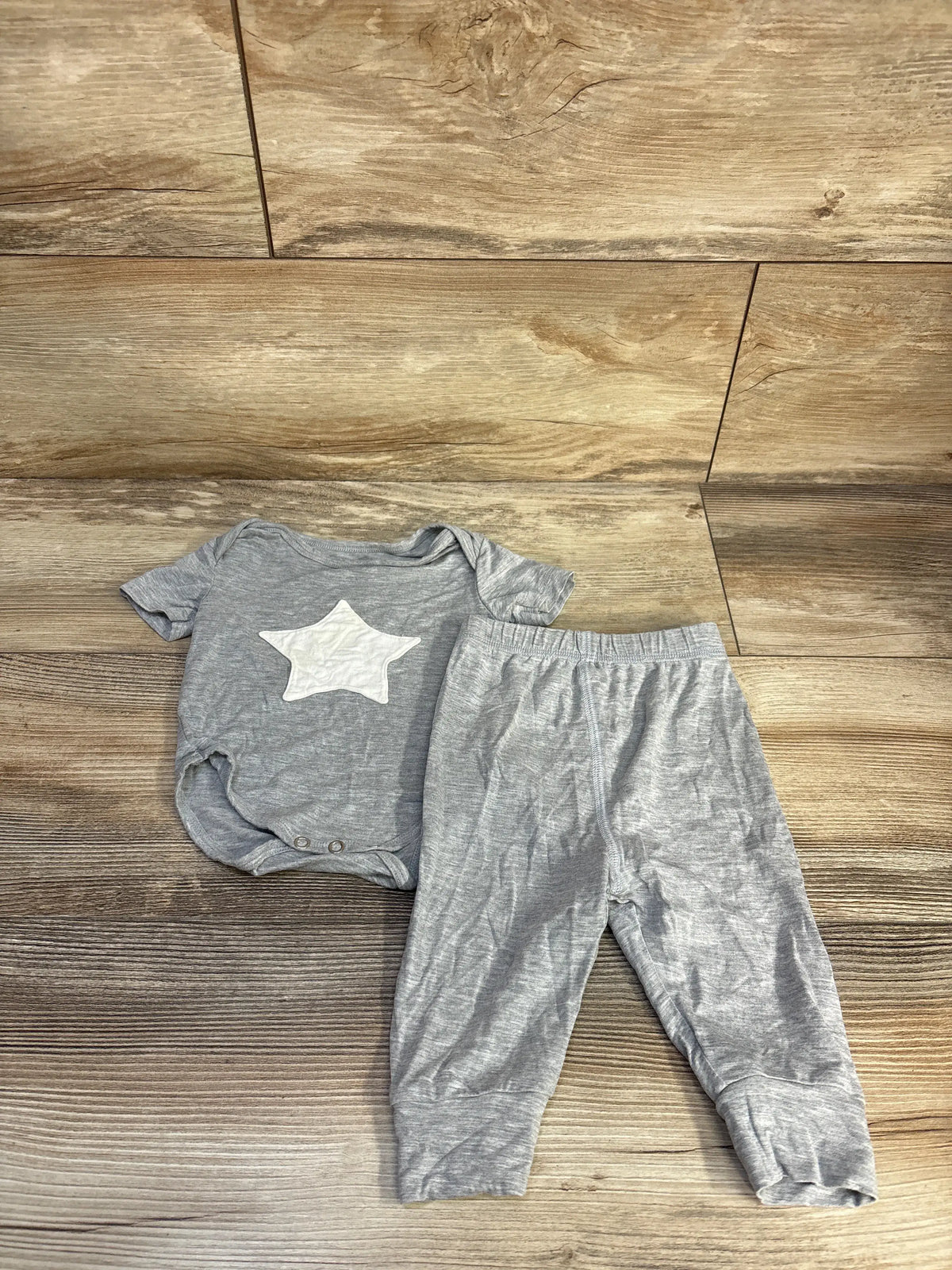 Top view of Earth Baby grey bamboo bodysuit and pants set showcasing a white star on the bodysuit against wood-grain flooring