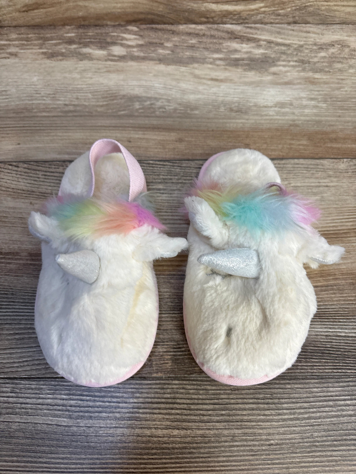 Soft unicorn slippers for kids with rainbow mane, pink trim, and glitter horn on wood floor