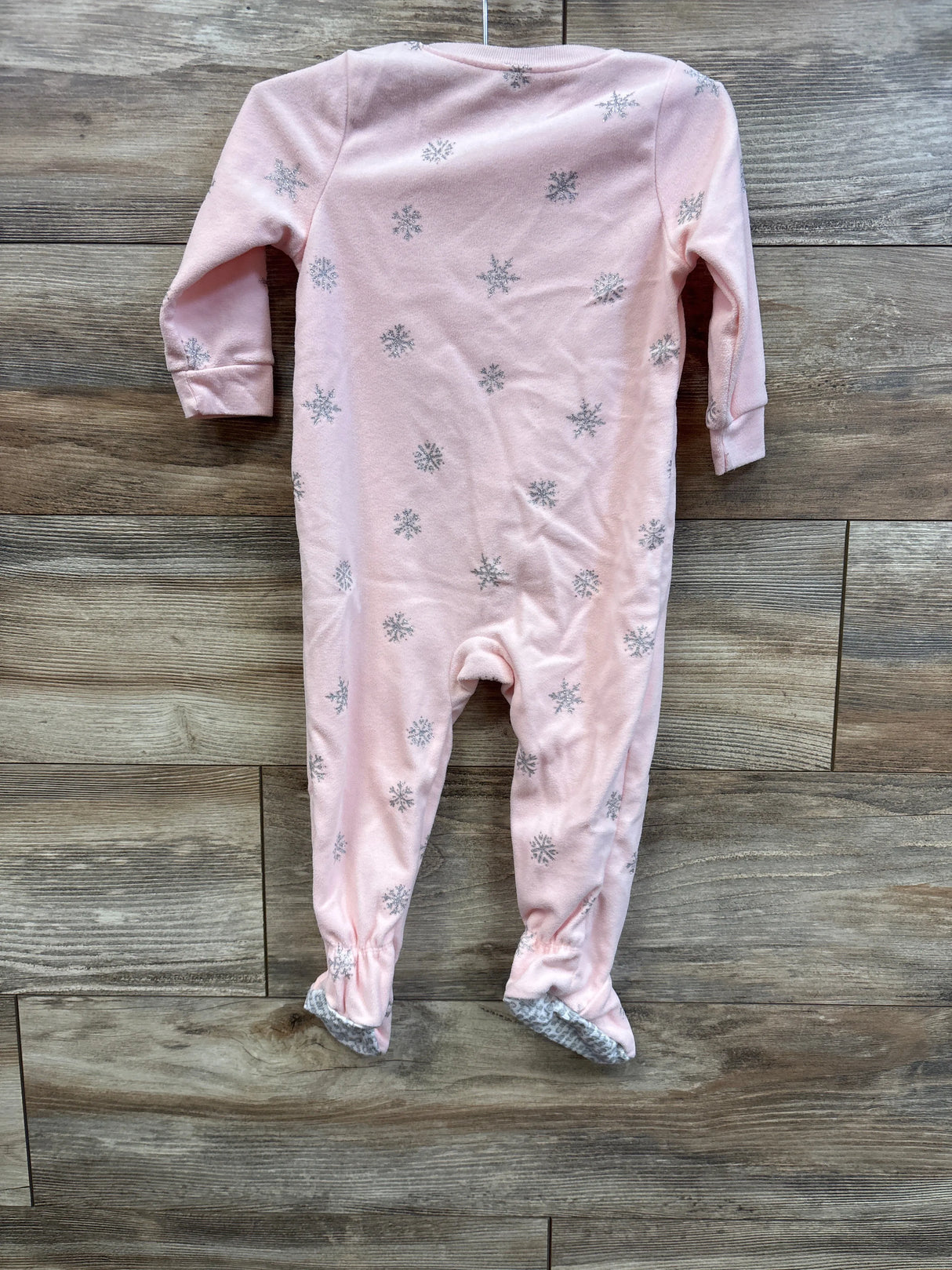 Back of pink Carter’s footed sleeper (18m) with silver snowflake print and grippy gray soles on wood background