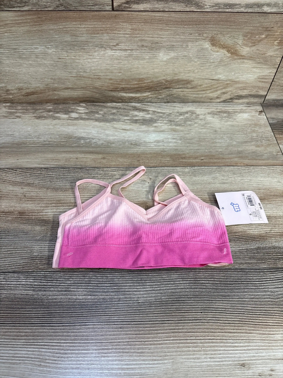 Pink ombre ribbed bralette with spaghetti straps on wood background, product tag attached