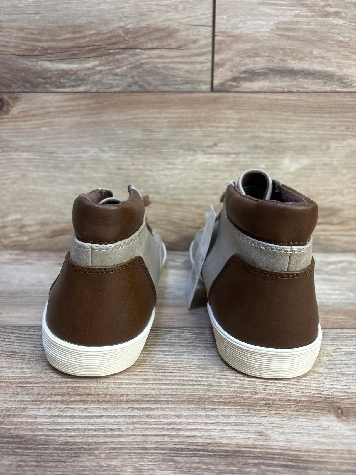 Brown and gray kids' high-top sneakers with white soles, viewed from the back on wood floor
