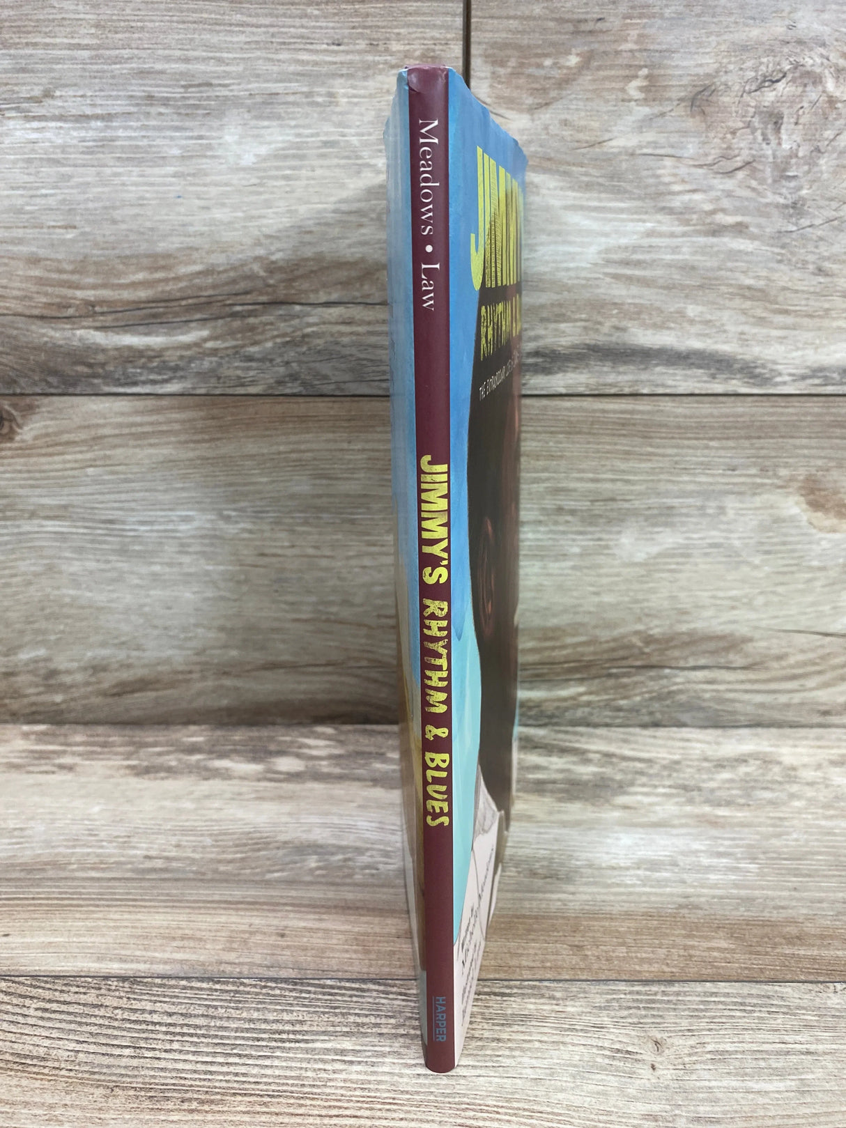 Spine view of Jimmy's Rhythm & Blues hardcover showing yellow title on maroon spine and slight top wear, wood background