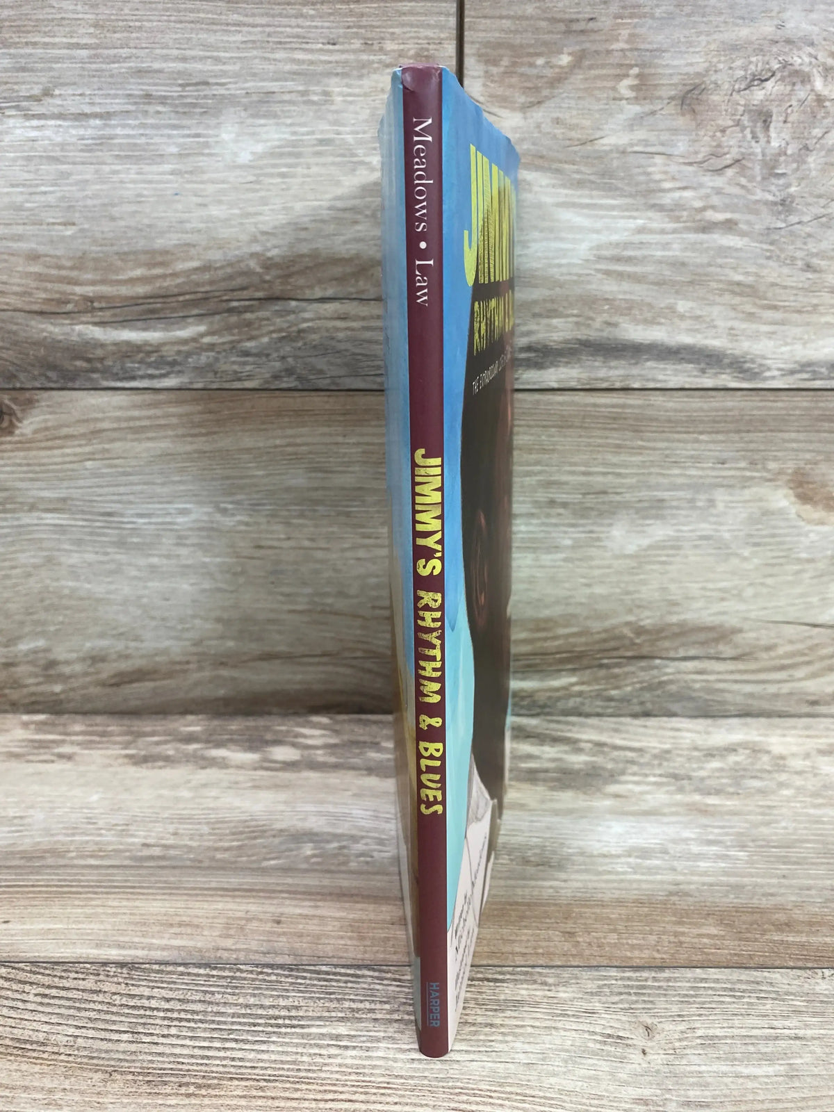 Spine view of Jimmy's Rhythm & Blues hardcover showing yellow title on maroon spine and slight top wear, wood background