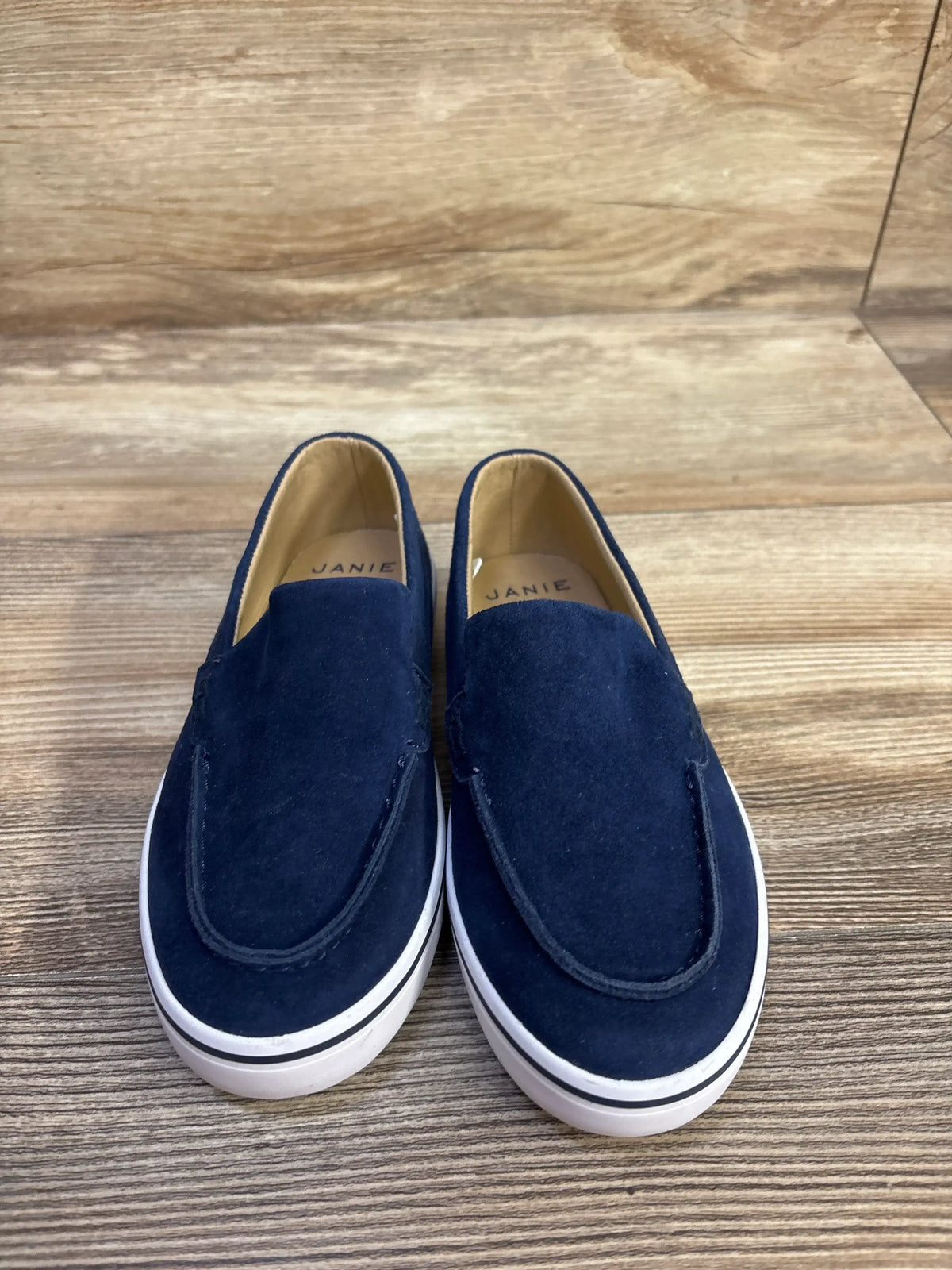 Front view of blue Janie & Jack suede slip-on sneakers showcasing white soles on a wood-grain floor
