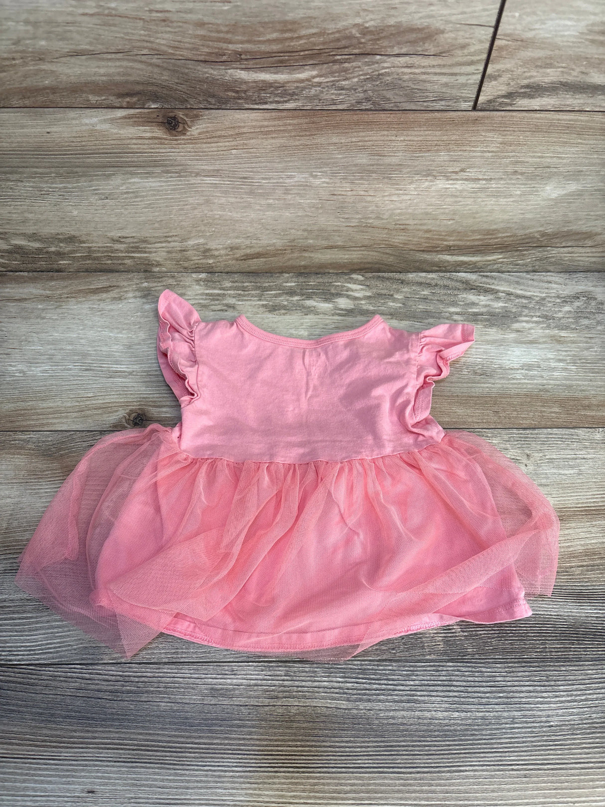 Pink baby dress with ruffle sleeves and tulle skirt on wood background