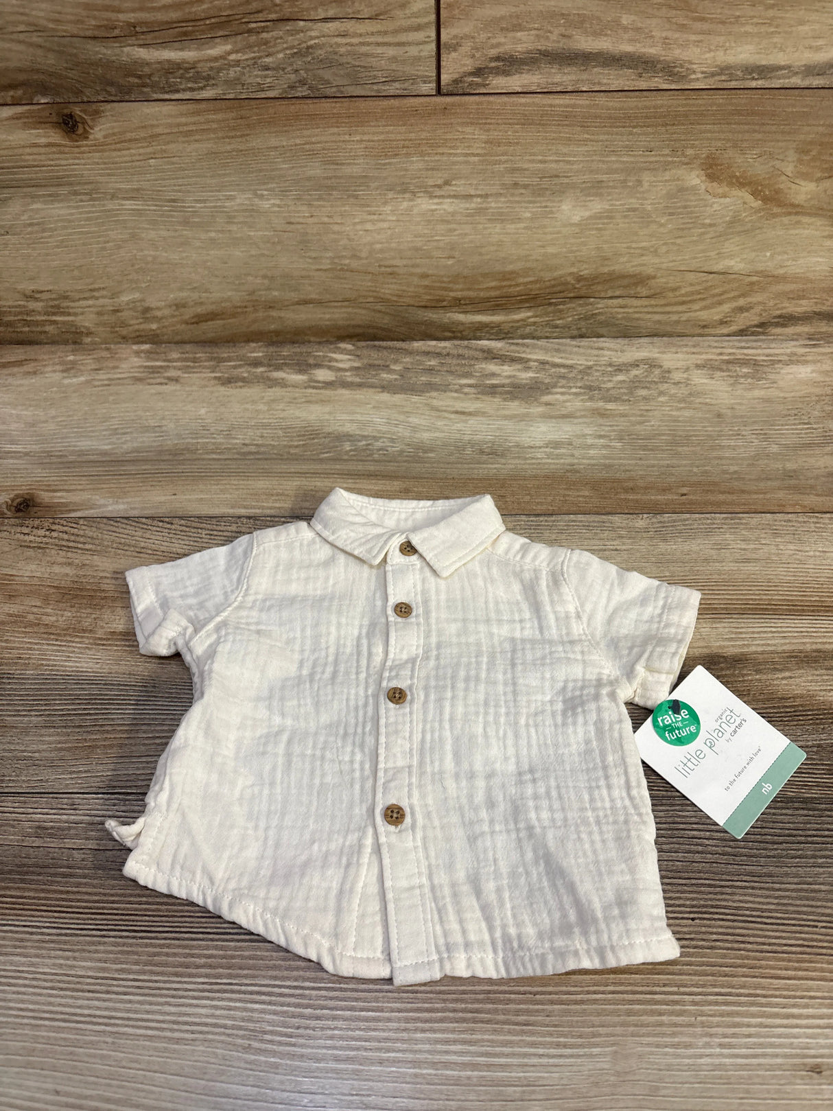 Flat lay of Little Planet newborn ivory organic muslin button-up shirt showing wooden buttons and collar on wood background