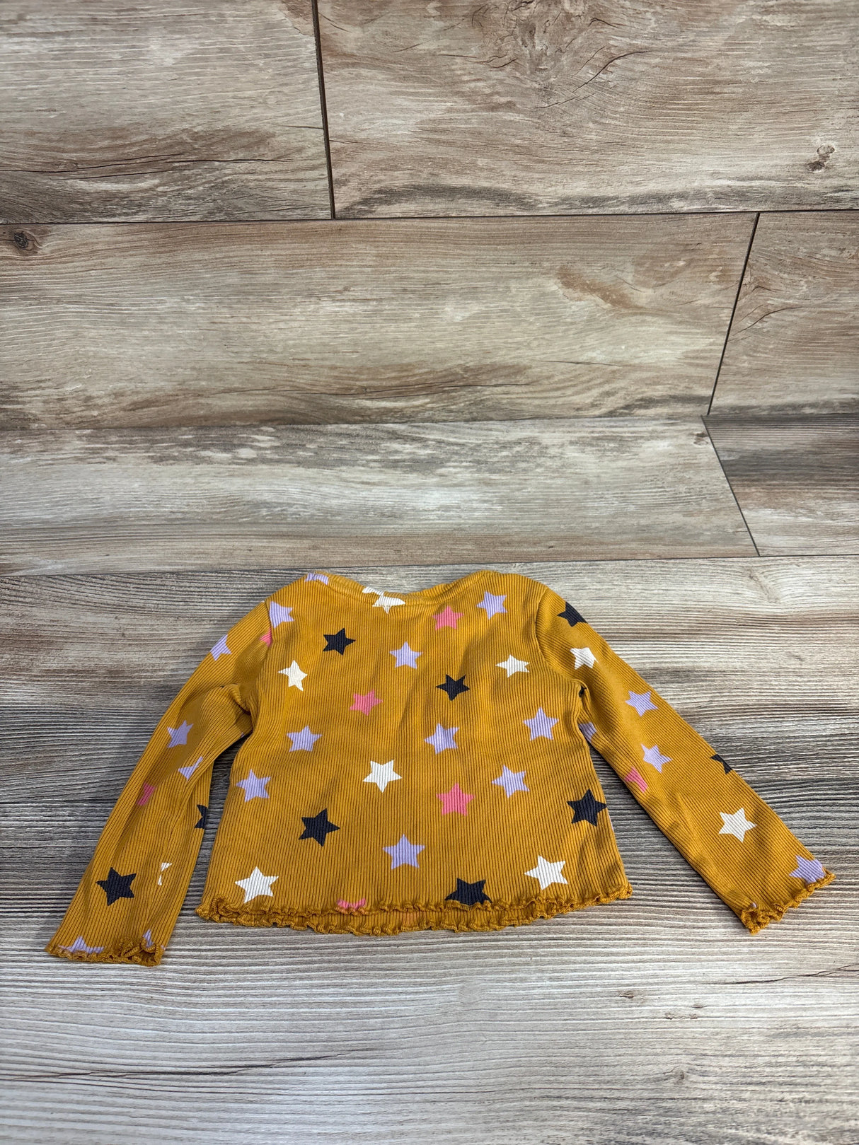 Mustard yellow long sleeve toddler shirt with multicolor star print on wood background