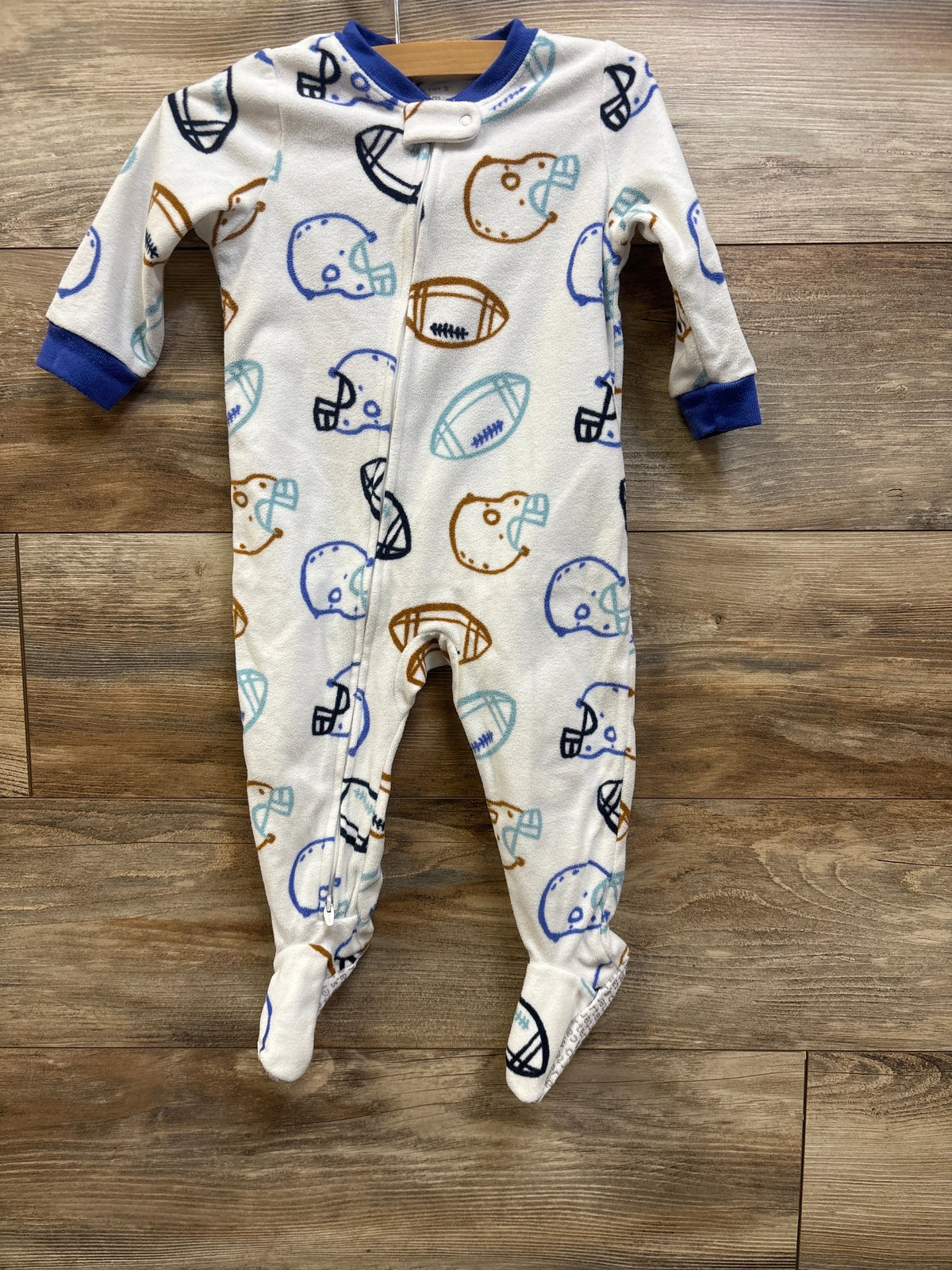 White Carter's football print baby blanket sleeper with blue trim on a wooden floor