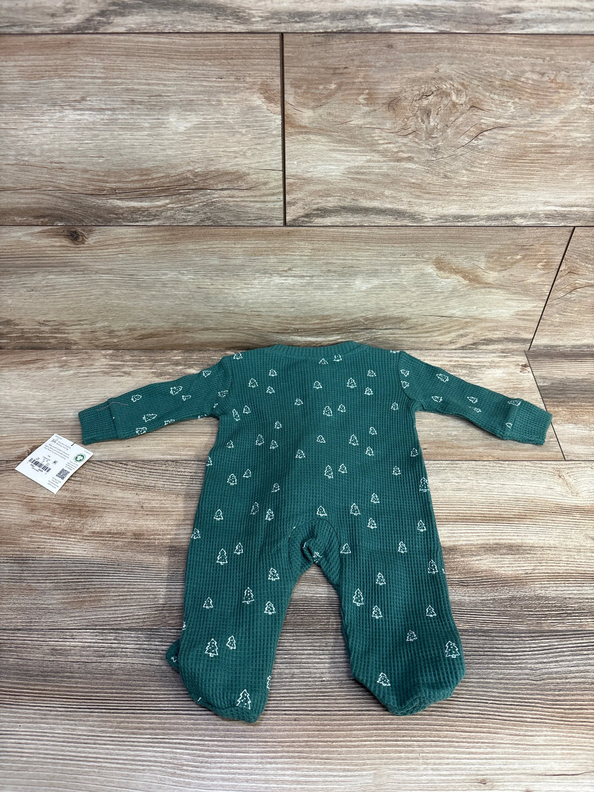 Green baby onesie with white tree pattern laid flat on wooden floor, long sleeves and footed legs