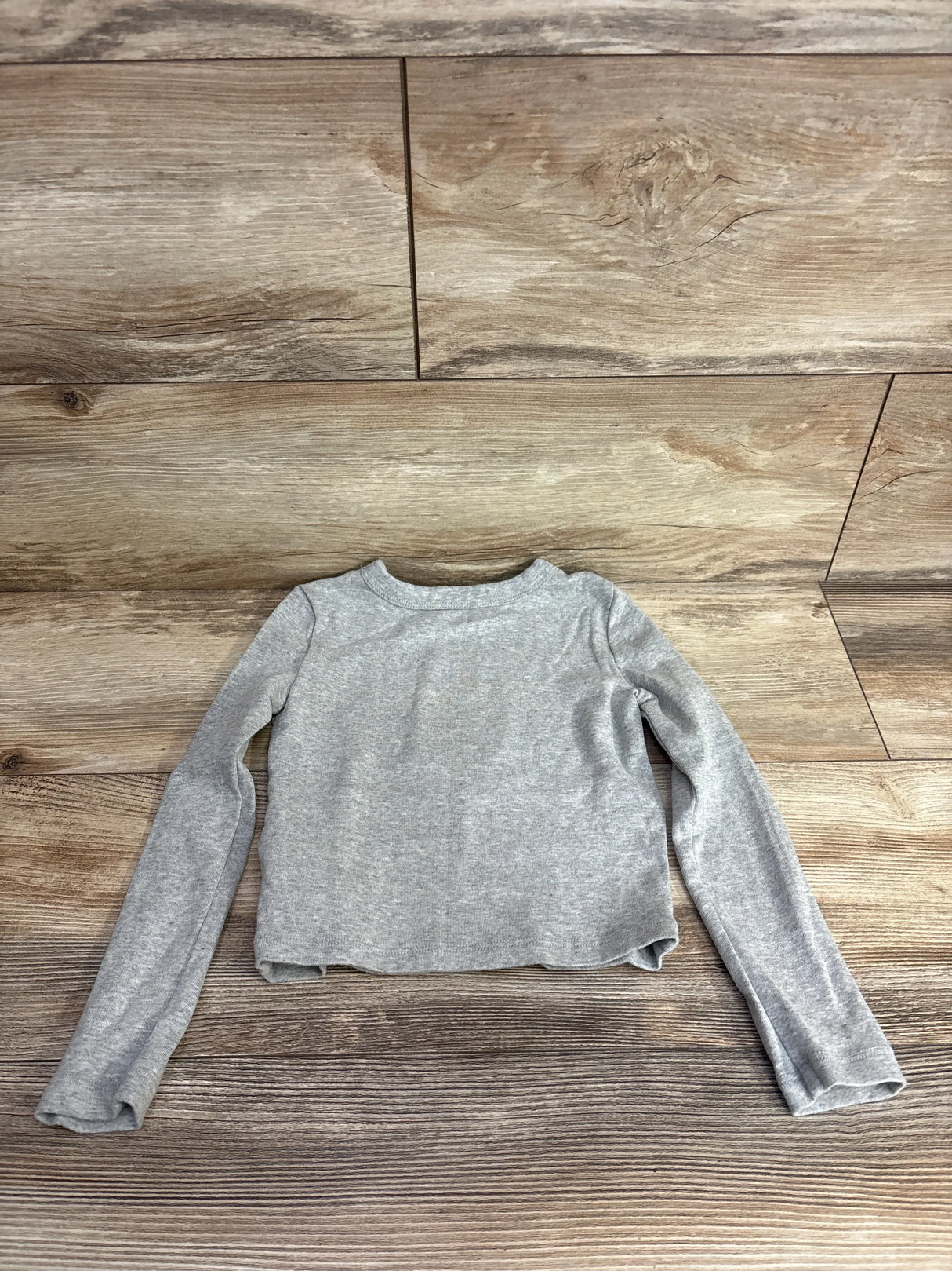 Light gray long sleeve kids shirt on wood background, children's clothing resale.
