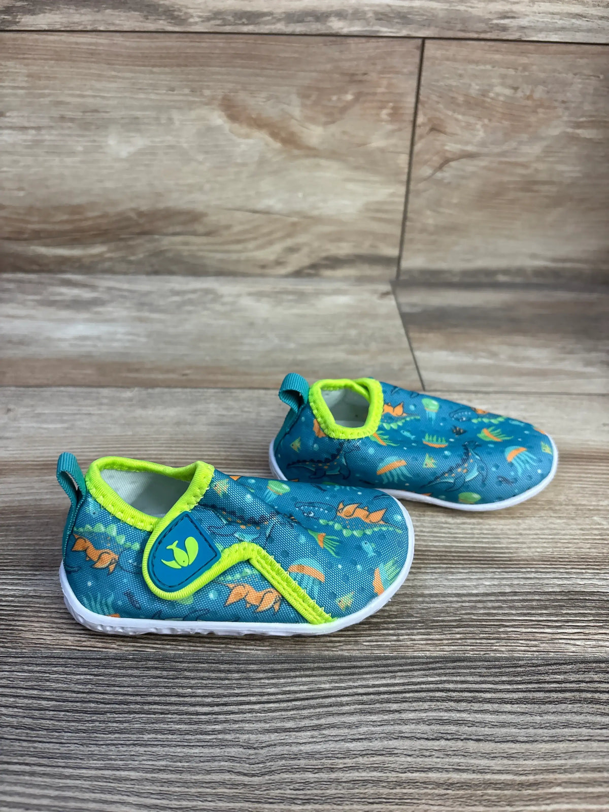 Side view of FEETCITY wide barefoot water shoes, teal size 4/5c, showcasing bright green trim and patterned uppers on a wood floor