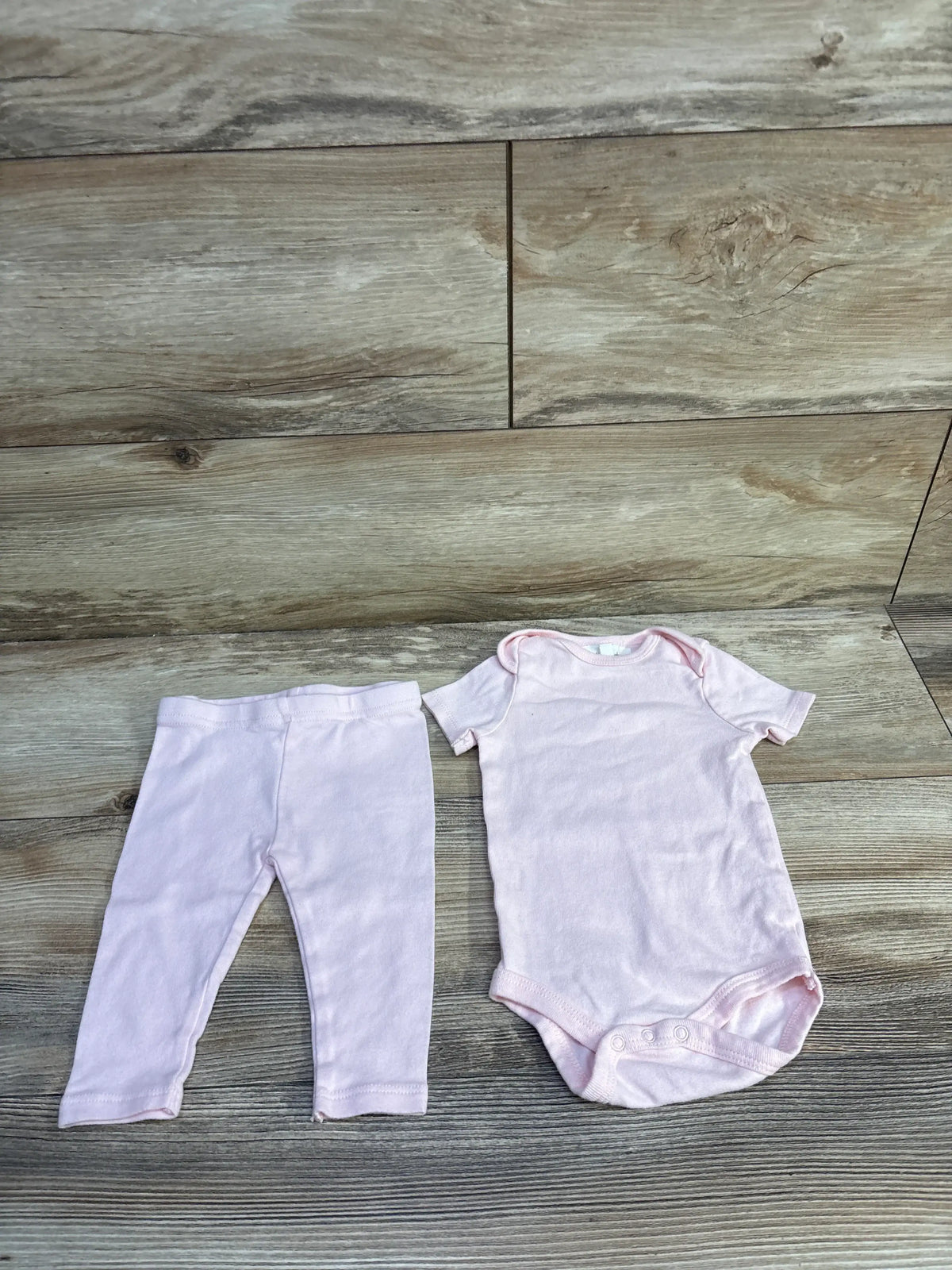 Front view of Starting Out pink two-piece set showing a short-sleeve bodysuit and matching pants on wood-look flooring