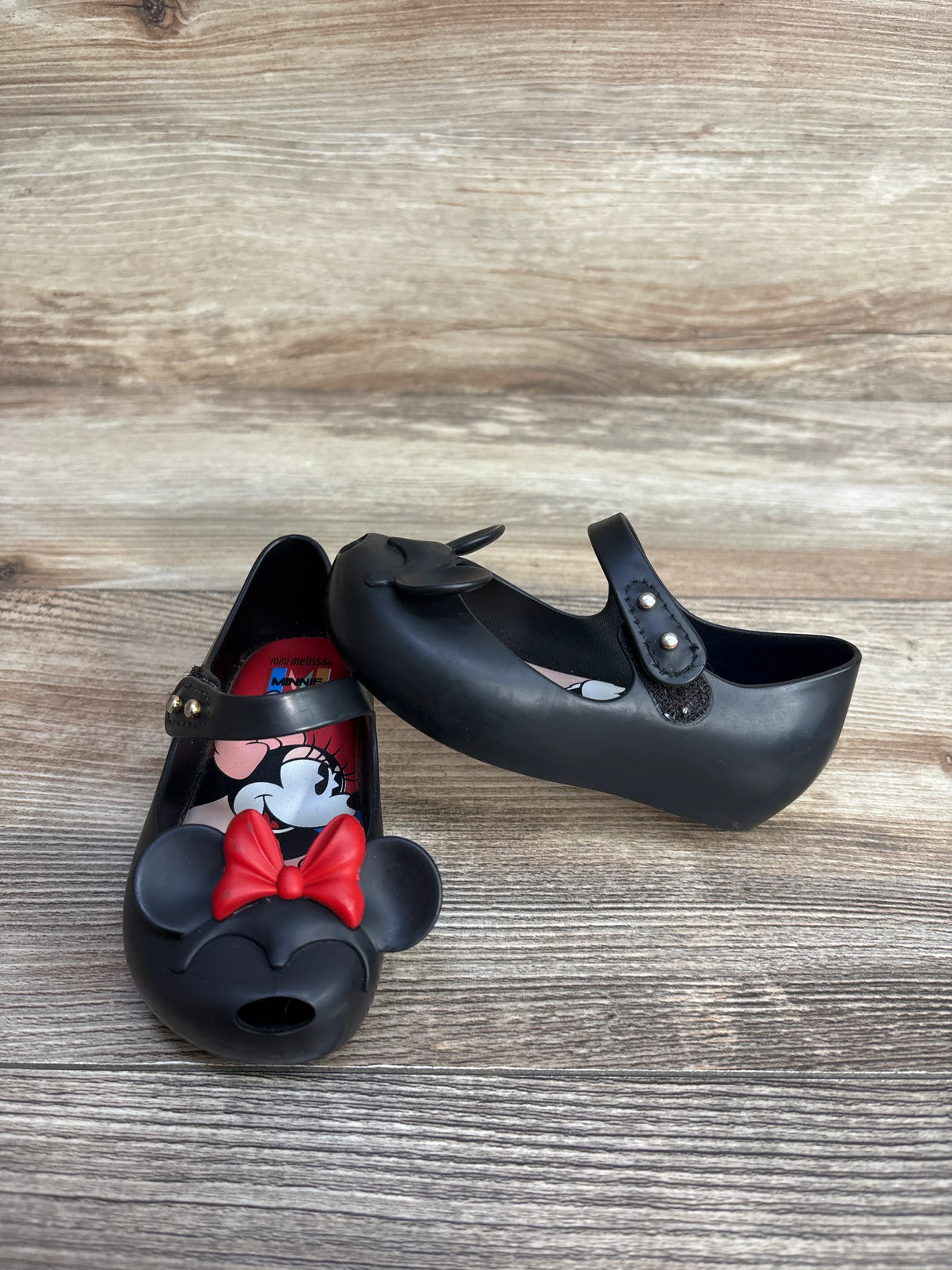 Black toddler Mary Jane shoes with Minnie Mouse face and red bow on wooden surface
