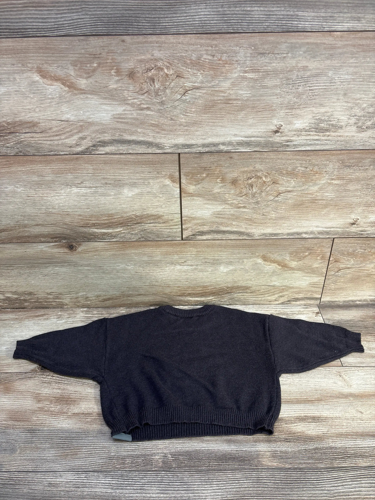 Flat lay of grey Modern Moments x Wicked toddler sweater with long sleeves and ribbed trim on a wood-look background