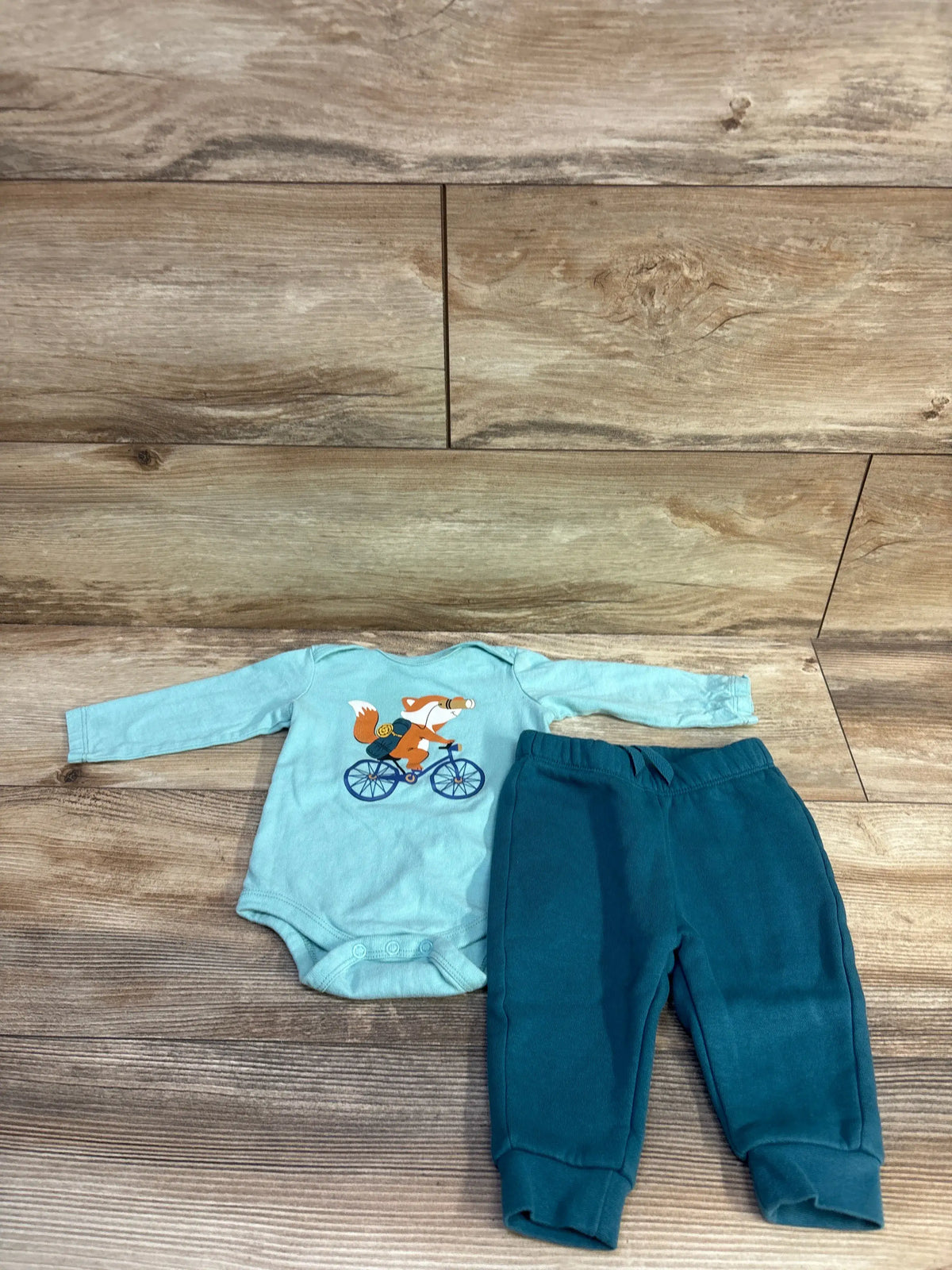 Top-down view of blue Koala Kids 2pc bodysuit and pants set with a fox bicycle graphic on wood