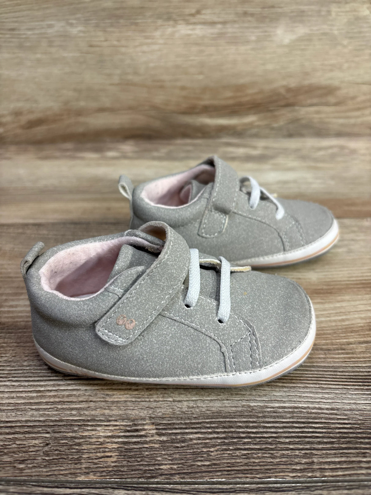 Pair of gray toddler shoes with white laces and hook-and-loop straps on wooden surface