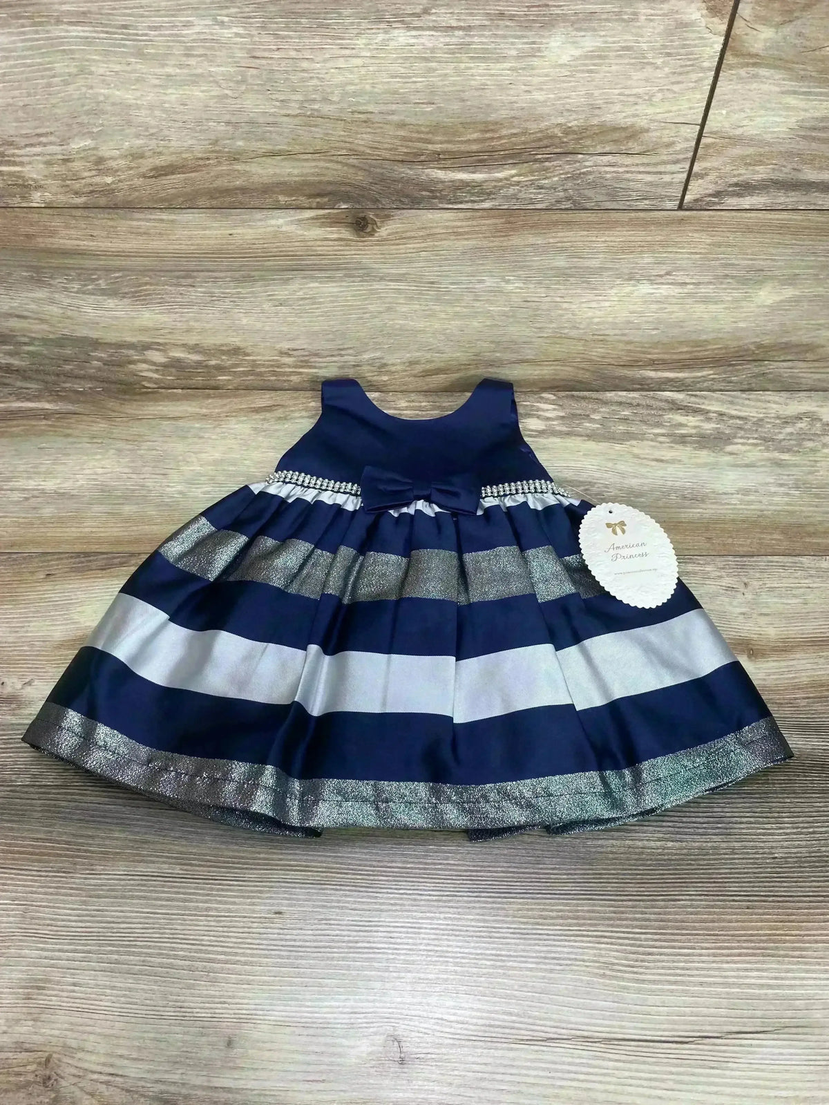 Flat lay of American Princess 2-piece navy sleeveless dress and bloomers with silver stripes and waist bow on wood backdrop