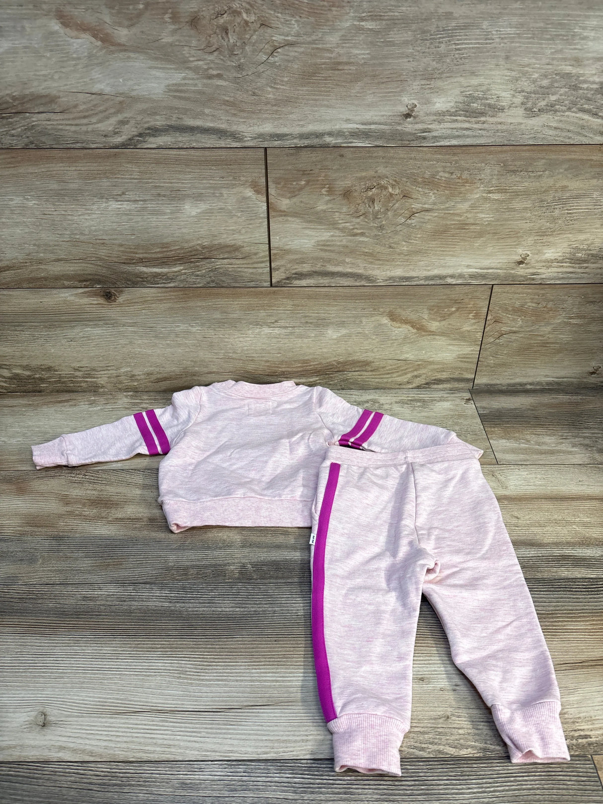Light pink toddler tracksuit with purple stripes, long sleeve top and matching pants on wood floor
