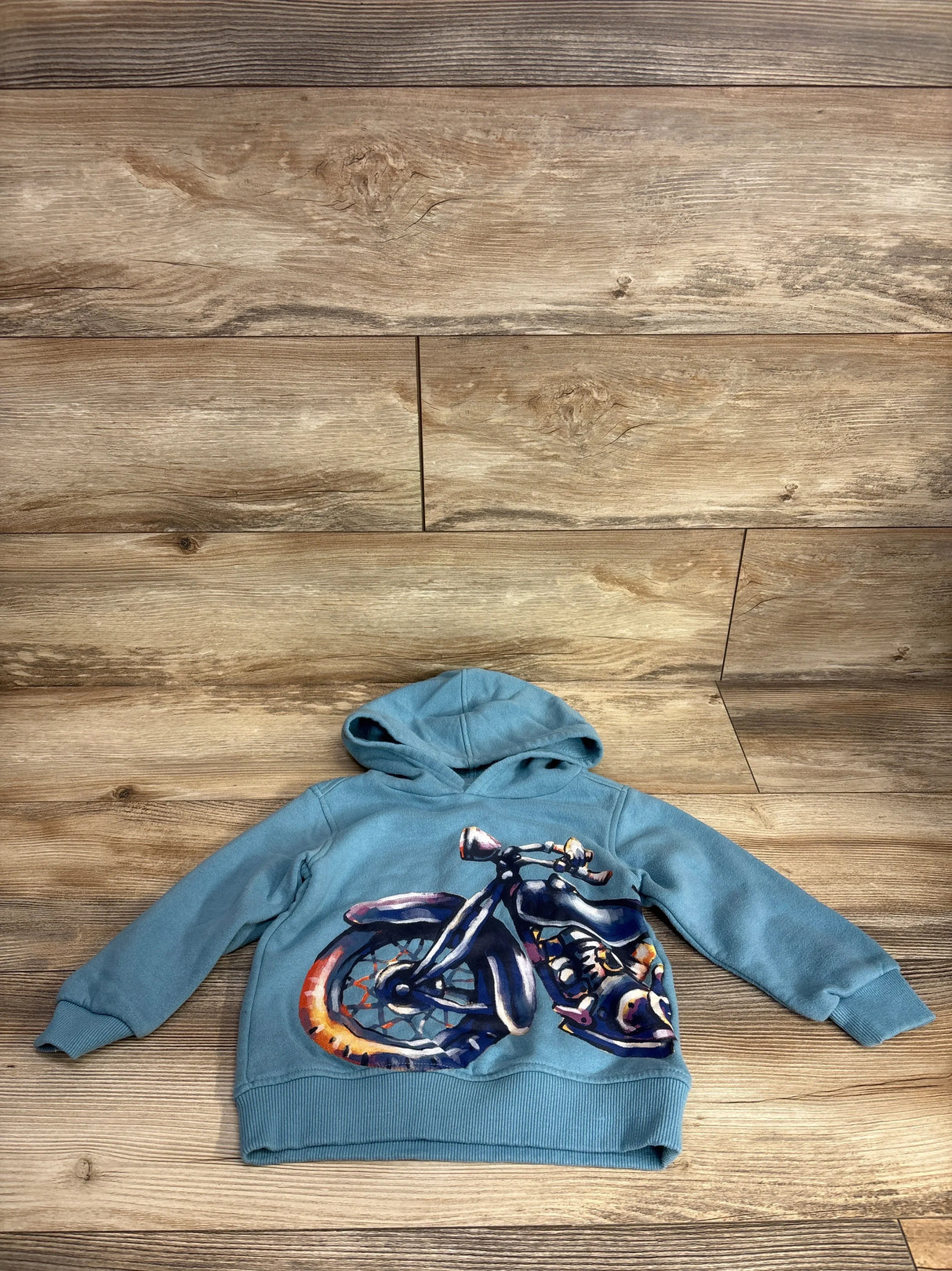 Blue kids hoodie with colorful motorcycle graphic on wooden background