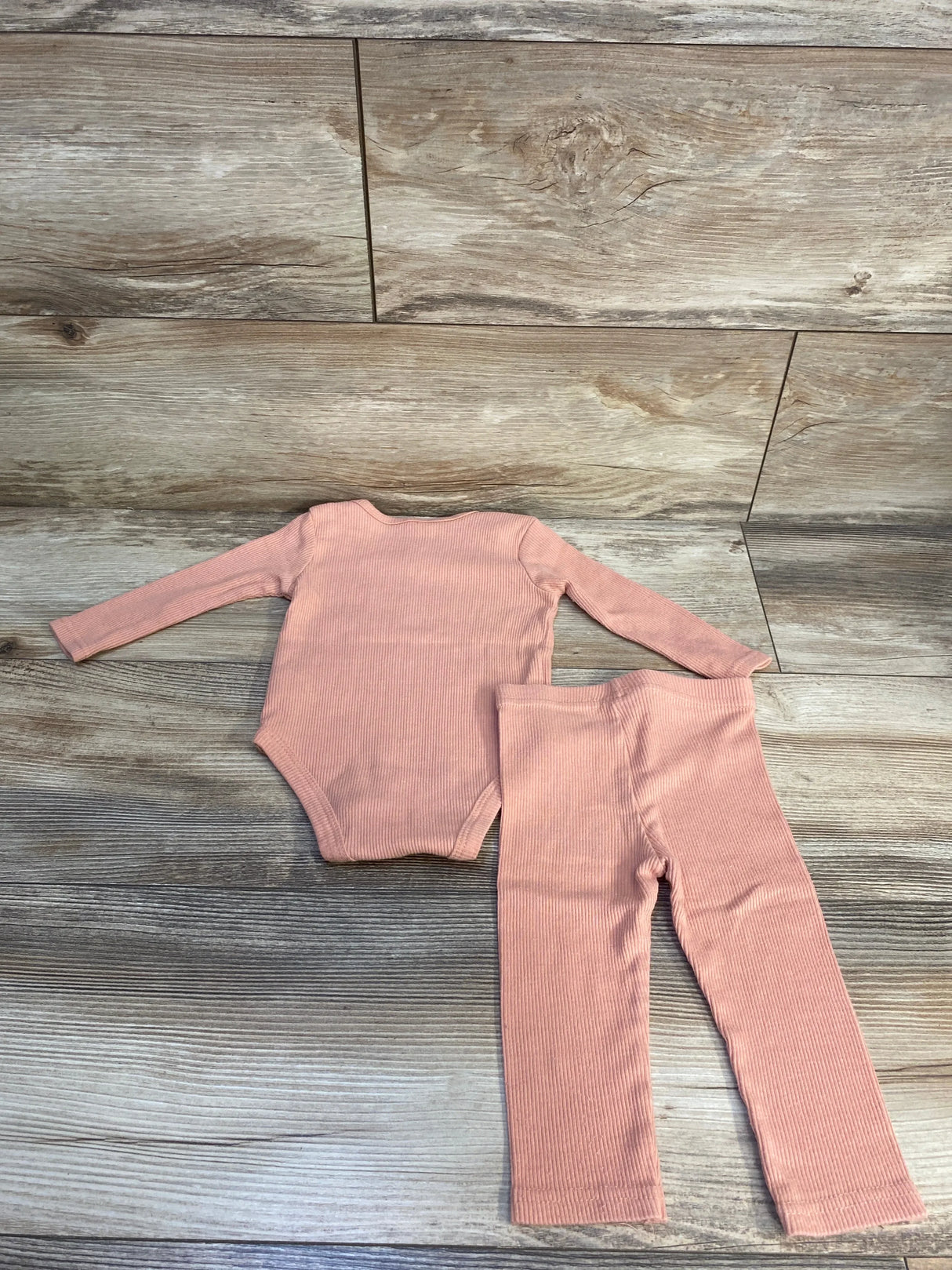 Pink ribbed baby bodysuit and matching pants set on wood background