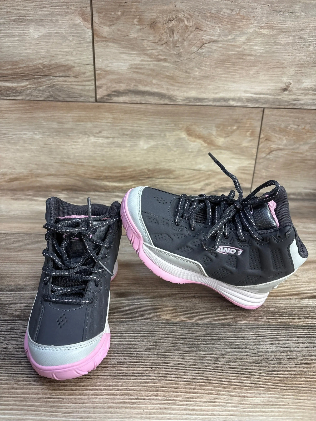Front and side view of AND1 Showout toddler basketball shoes in dark gray with pink soles, lace-up high-top on wood floor
