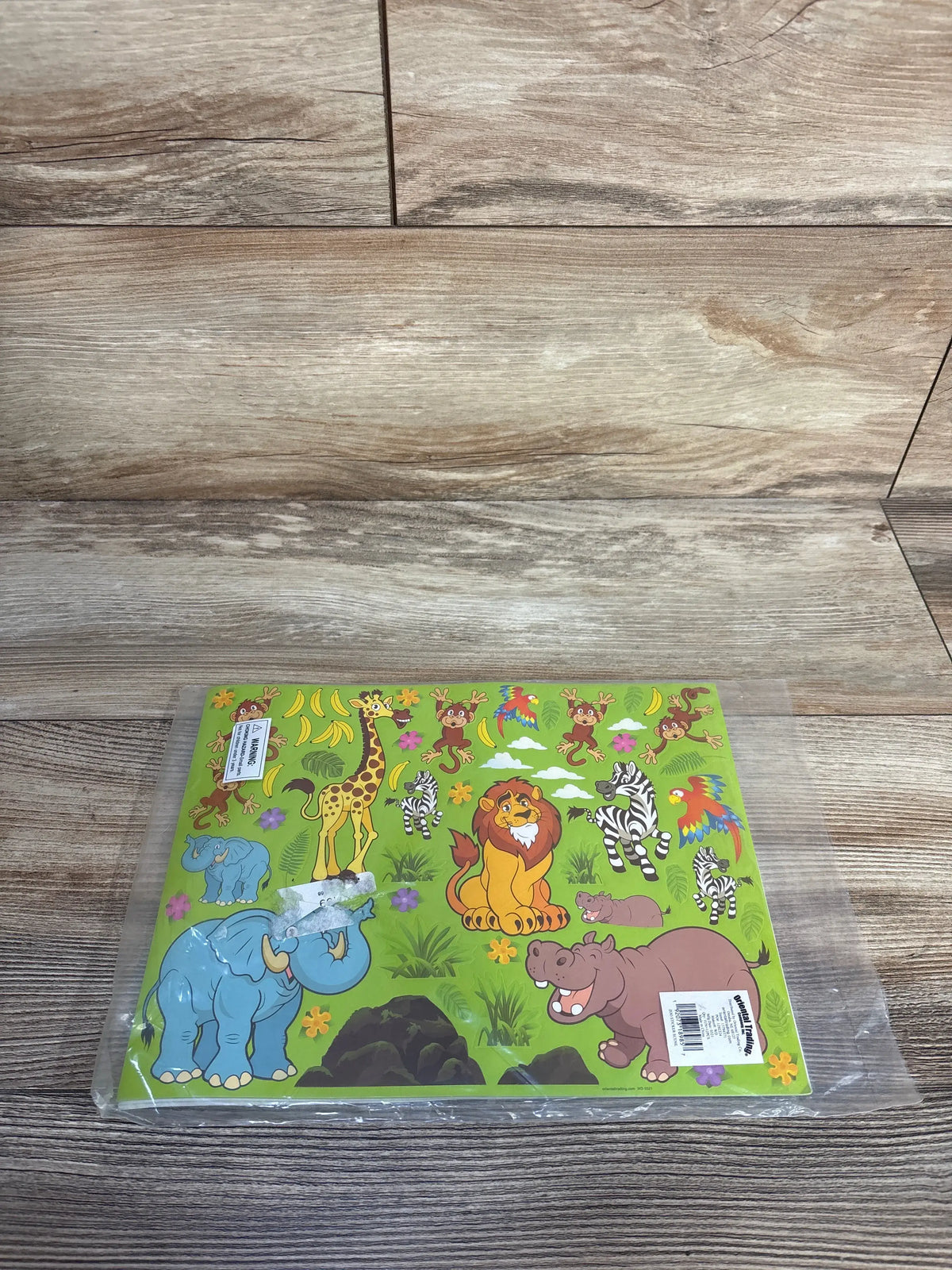 Front view of zoo sticker sheet in plastic sleeve showing colorful cartoon animals: lion, elephant, hippo, giraffe, zebras, monkeys and parrot on green background