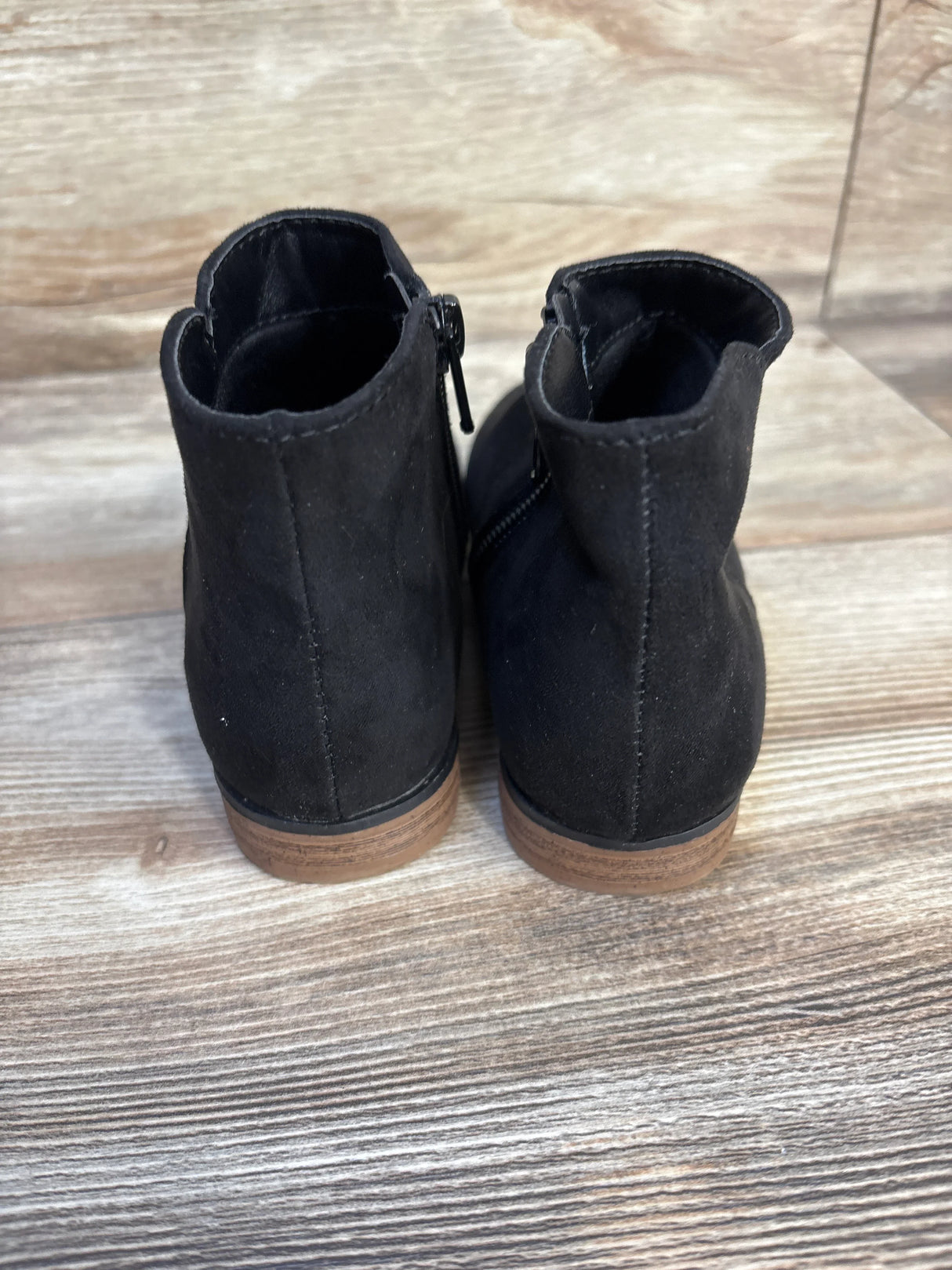 Back view of black kids ankle boots with brown soles on wood floor