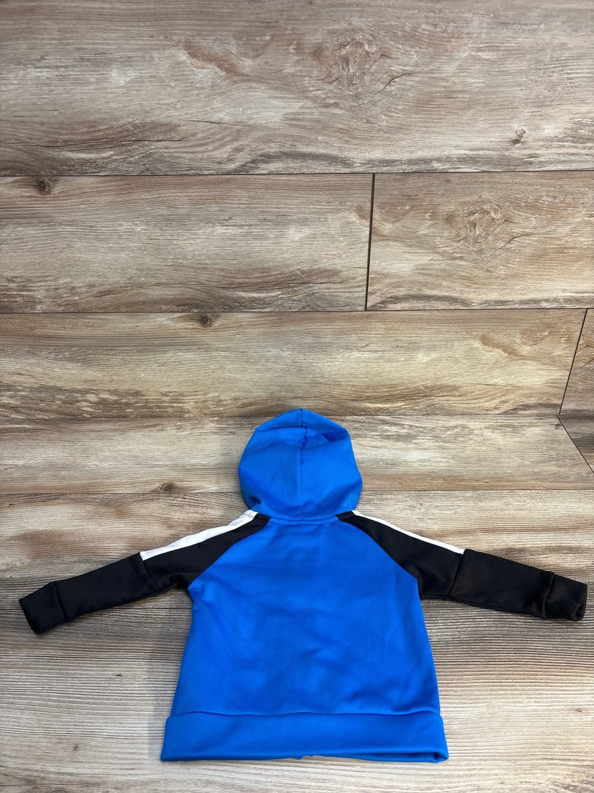 Blue and black kids hoodie with white shoulder stripes laid flat on wooden floor