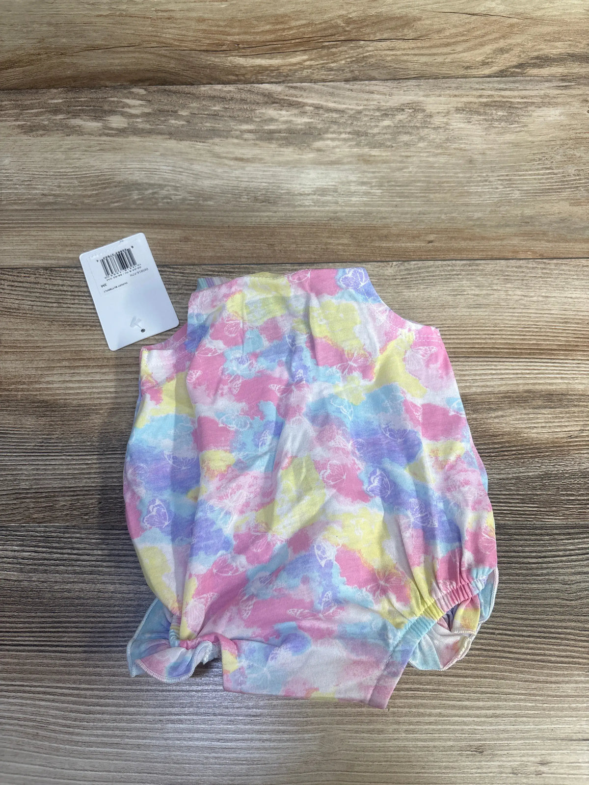 Top view of pink Hurley butterfly bubble romper showcasing pastel butterfly print and flutter sleeves on a wood surface