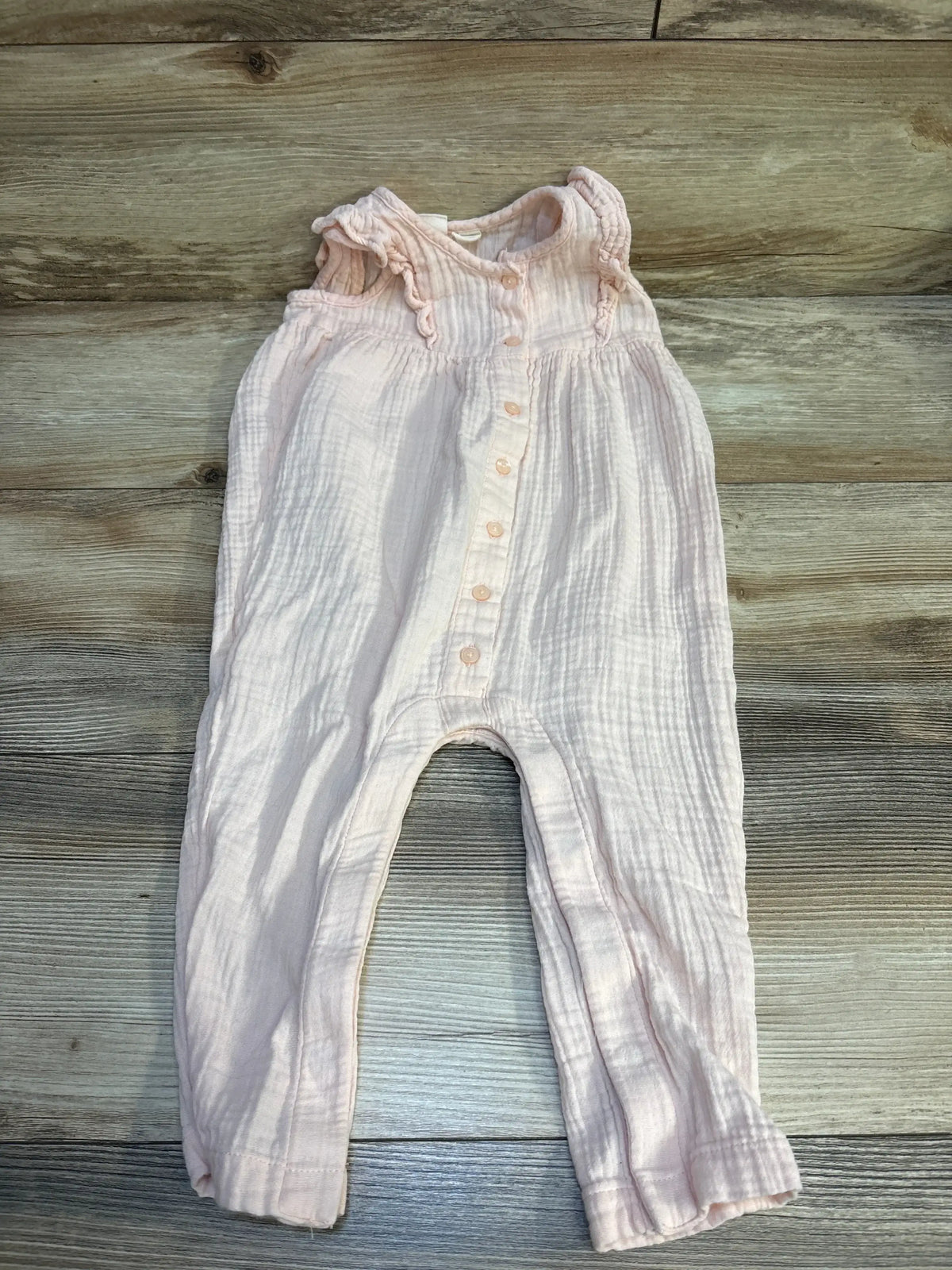 Pink baby romper with ruffled sleeves and button front on wood background