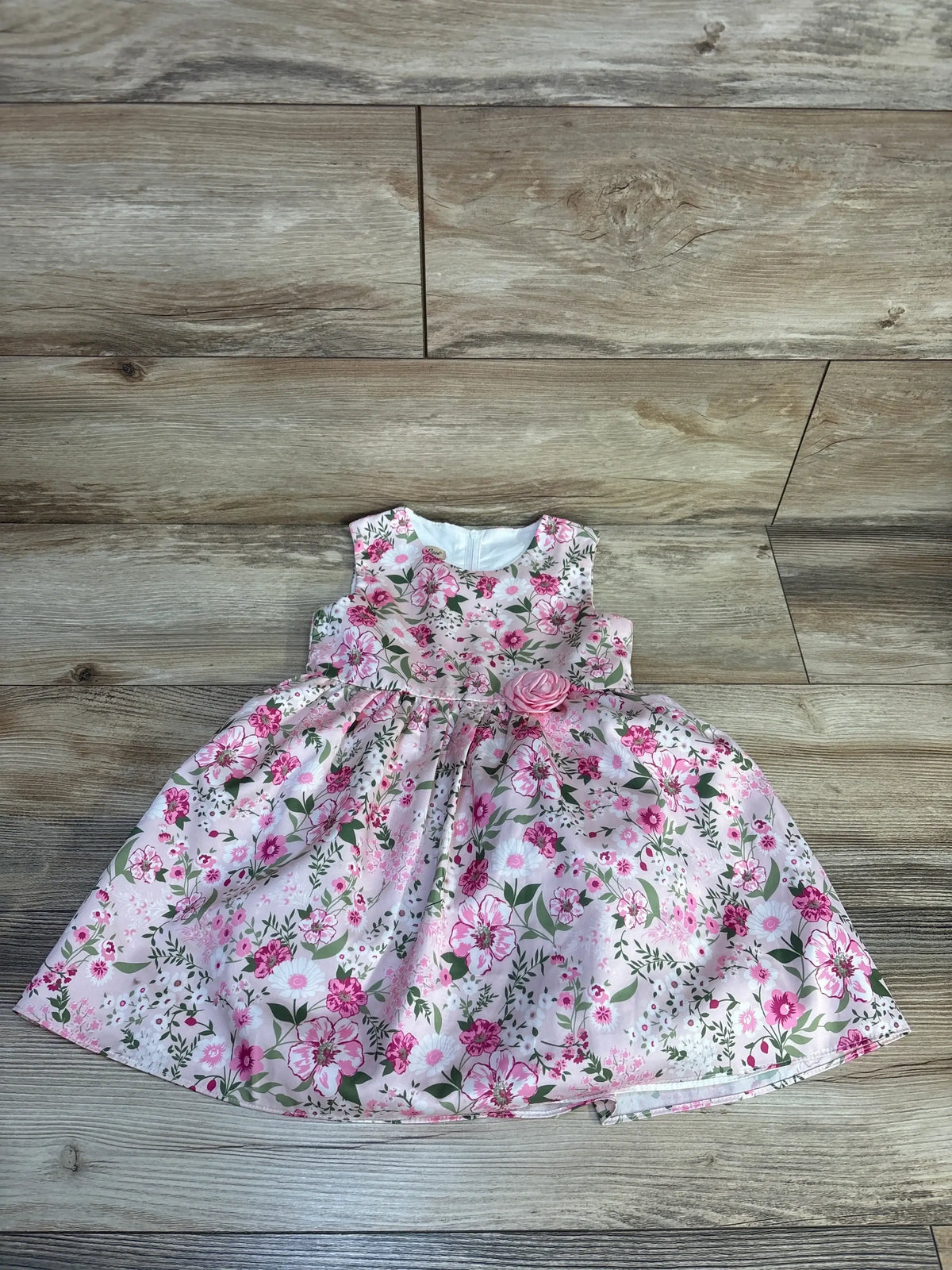 Pink floral baby dress with flower accent, sleeveless, laid flat on wooden background
