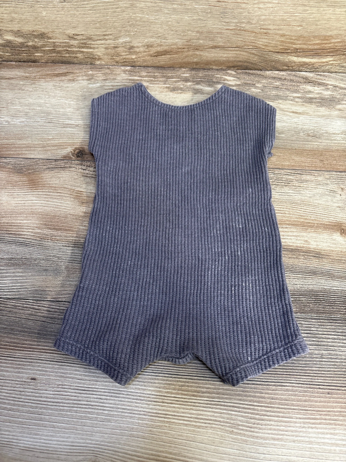 Flat lay of grey Grayson romper showing ribbed knit, cap sleeves, scalloped legs on light wood background