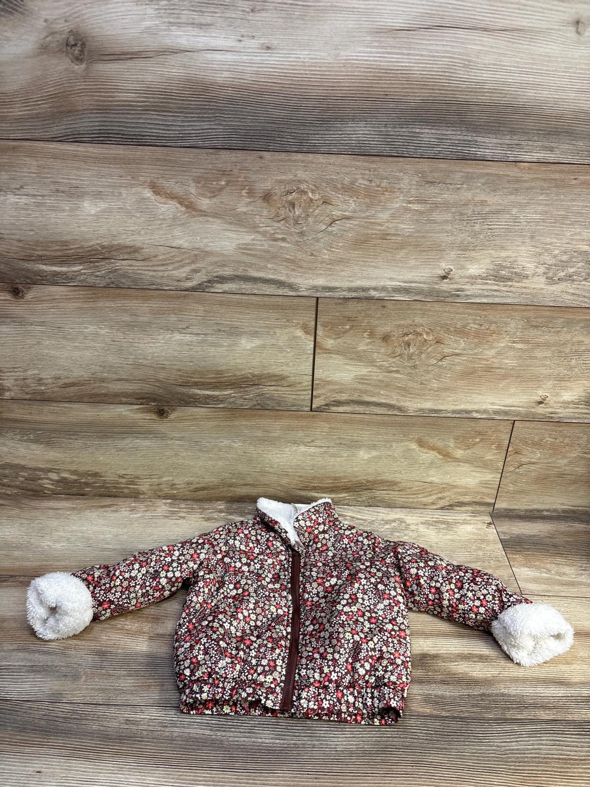 Front view of floral full-zip lined baby jacket showcasing maroon-brown print and white sherpa-lined collar and cuffs on wood background