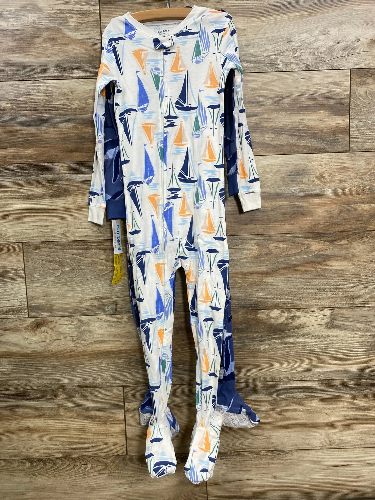 Baby footed pajamas with sailboat print in blue, orange, and green, hanging on wooden floor