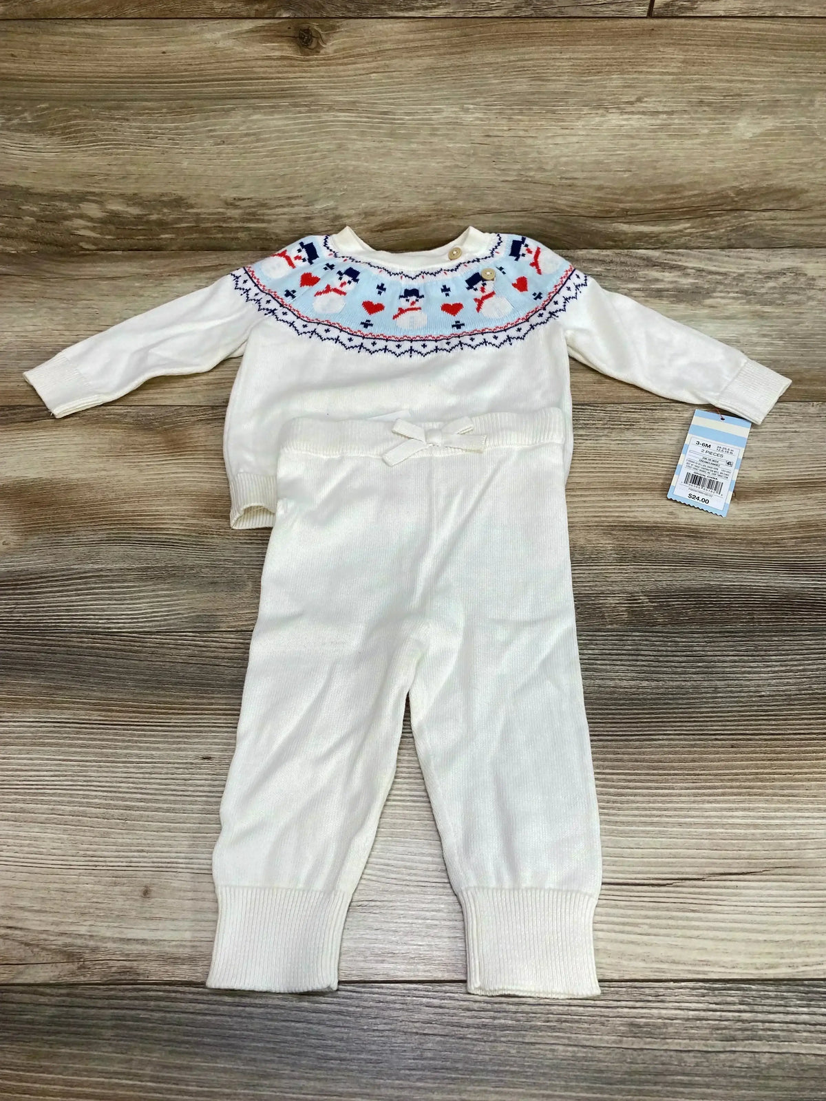 Flat lay of white Cat & Jack two-piece baby sweater set 3-6M showing snowman Fair Isle yoke and ribbed cuffs on wood background