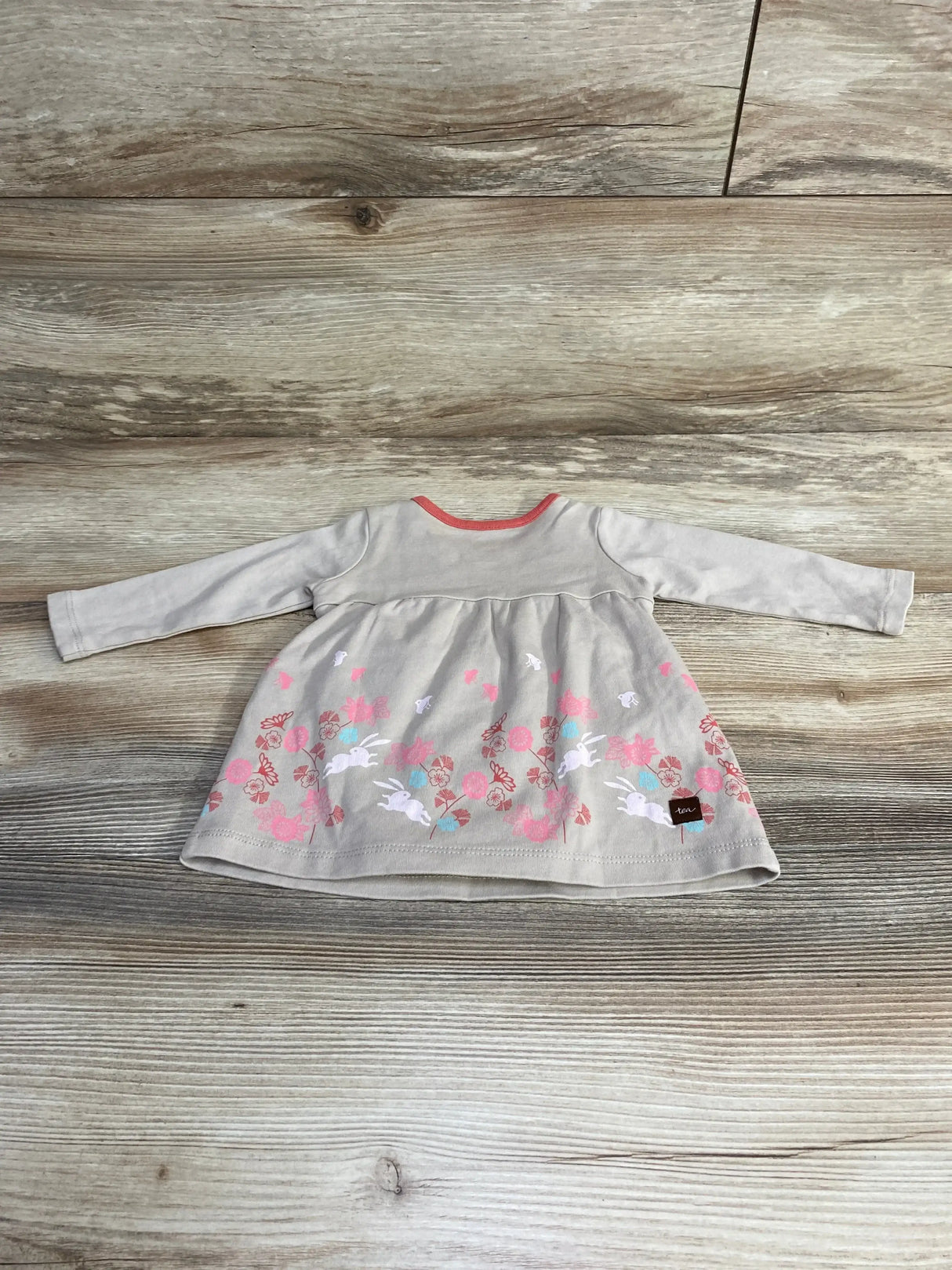 Flat lay of NWOT Tea Collection grey long sleeve dress showcasing bunny and floral print with coral trim on a wood plank floor