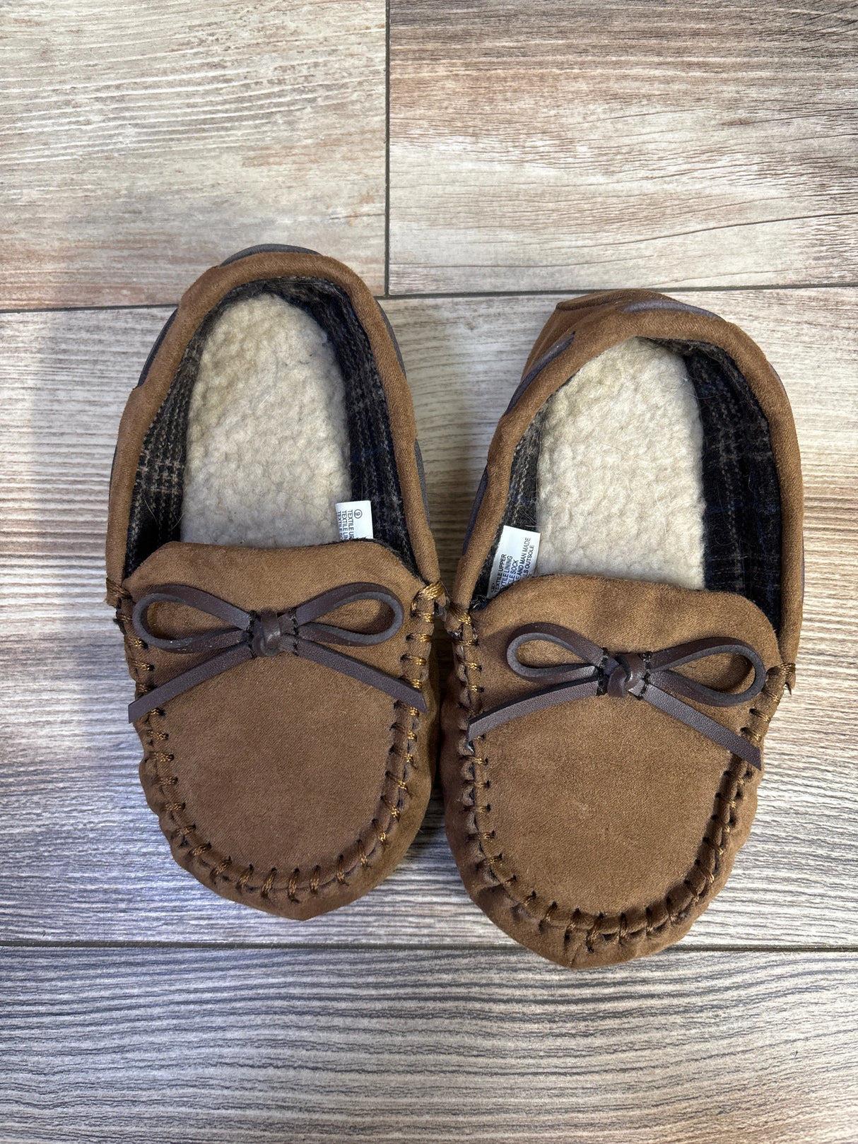 Top view of Cat & Jack toddler brown moccasin slippers showing faux-shearling lining, stitched suede upper and bow on wood floor
