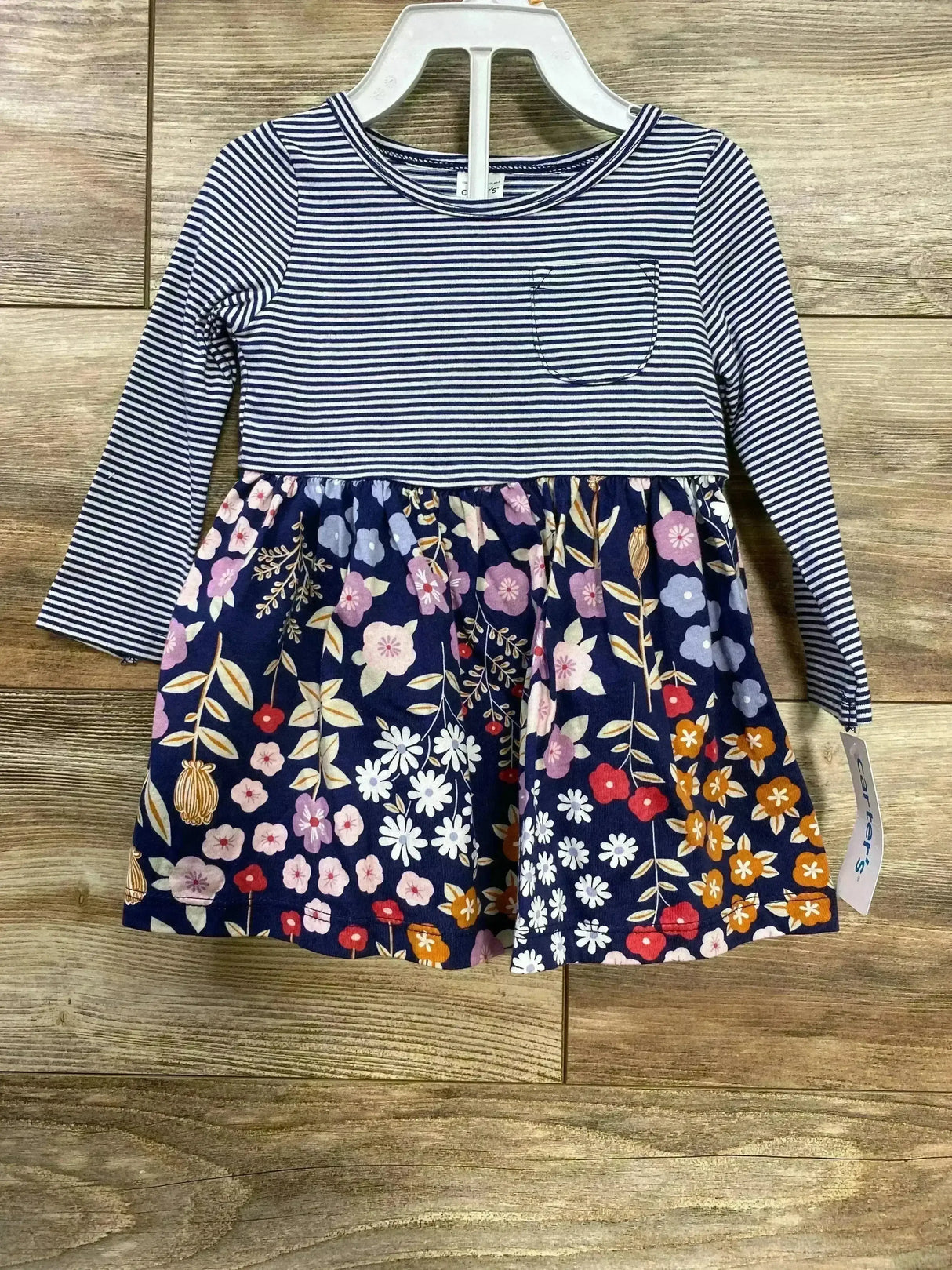 Front view of Carters navy 2-piece baby dress with striped long sleeves and floral skirt on hanger against wood background